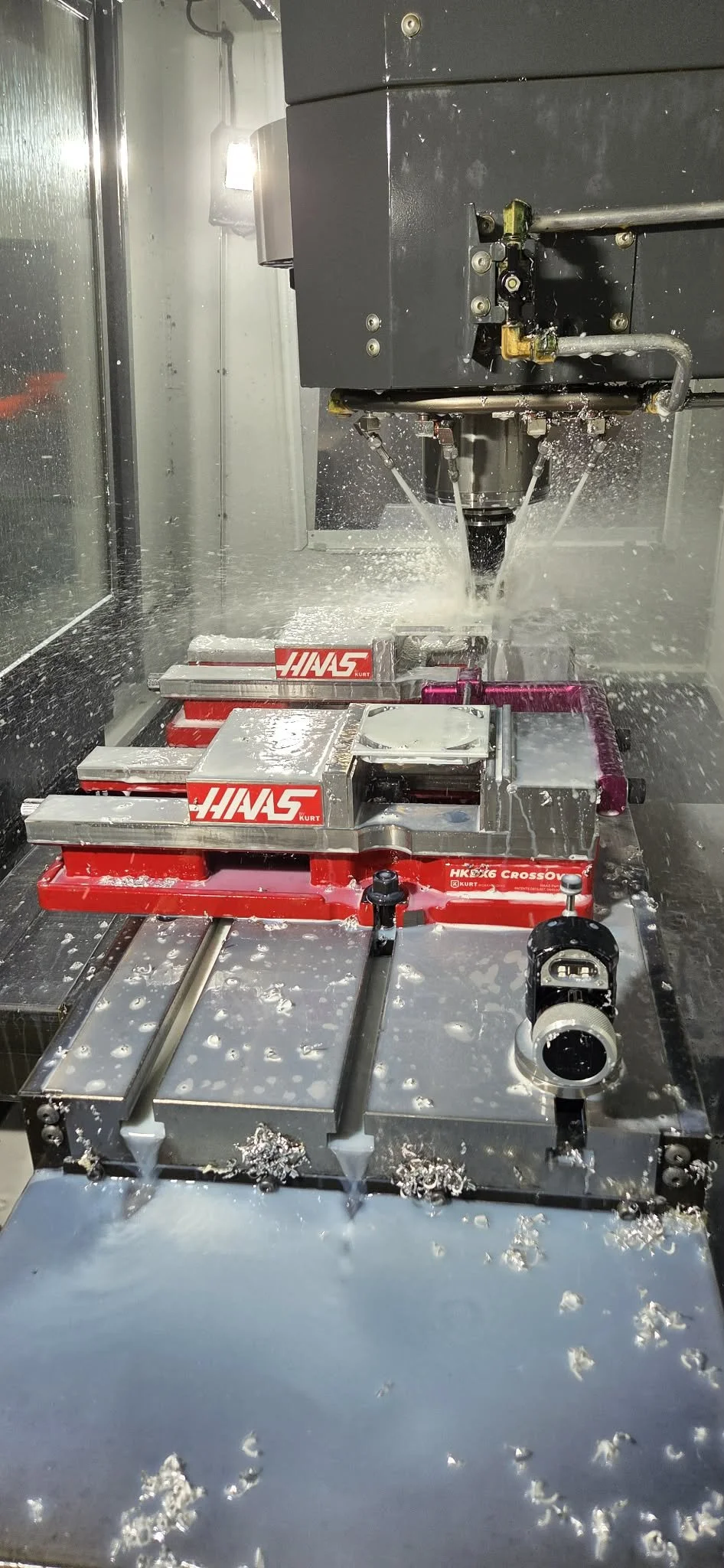 A CNC machine carving or milling metal parts, with metal shavings and coolant fluid visible around the work area.