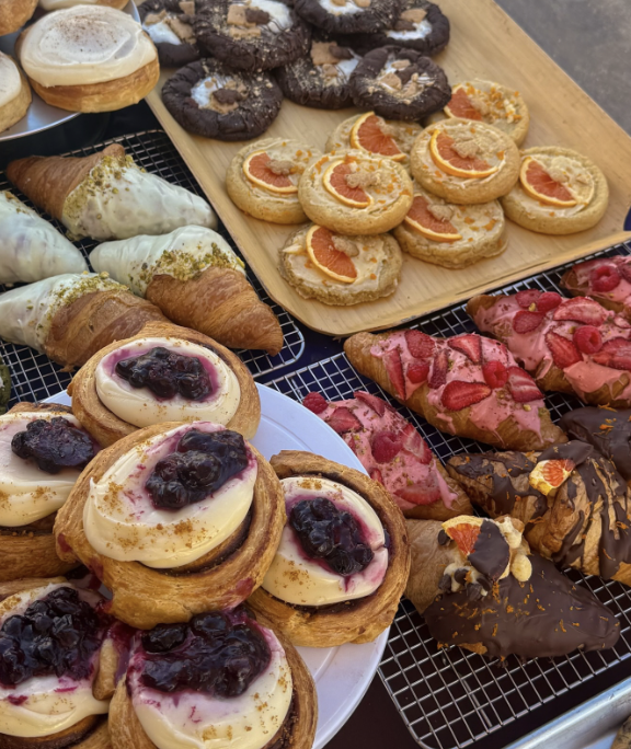Assorted desserts including cookies, croissants, Danish pastries with fruit and chocolate toppings, and donut-like treats with icing and fruit toppings.