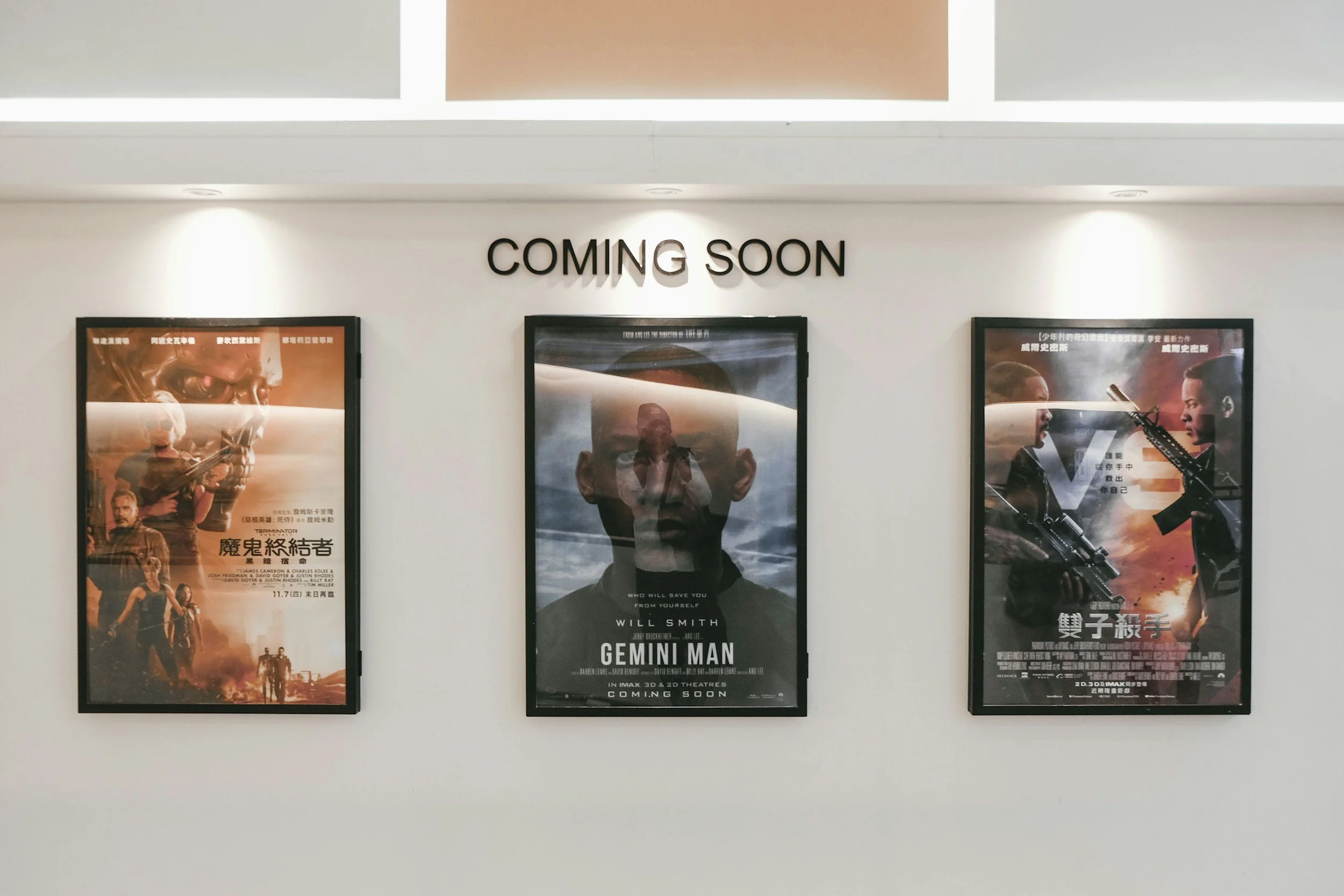 Three movie posters on a white wall with a sign above that reads "COMING SOON." The posters feature science fiction and action themes, with images of characters and scenes from the movies.