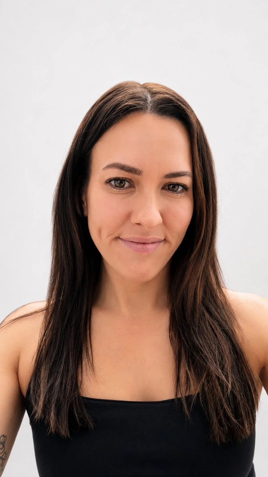 A woman with long brown hair and light skin, wearing a black tank top, smiling gently at the camera against a plain white background.