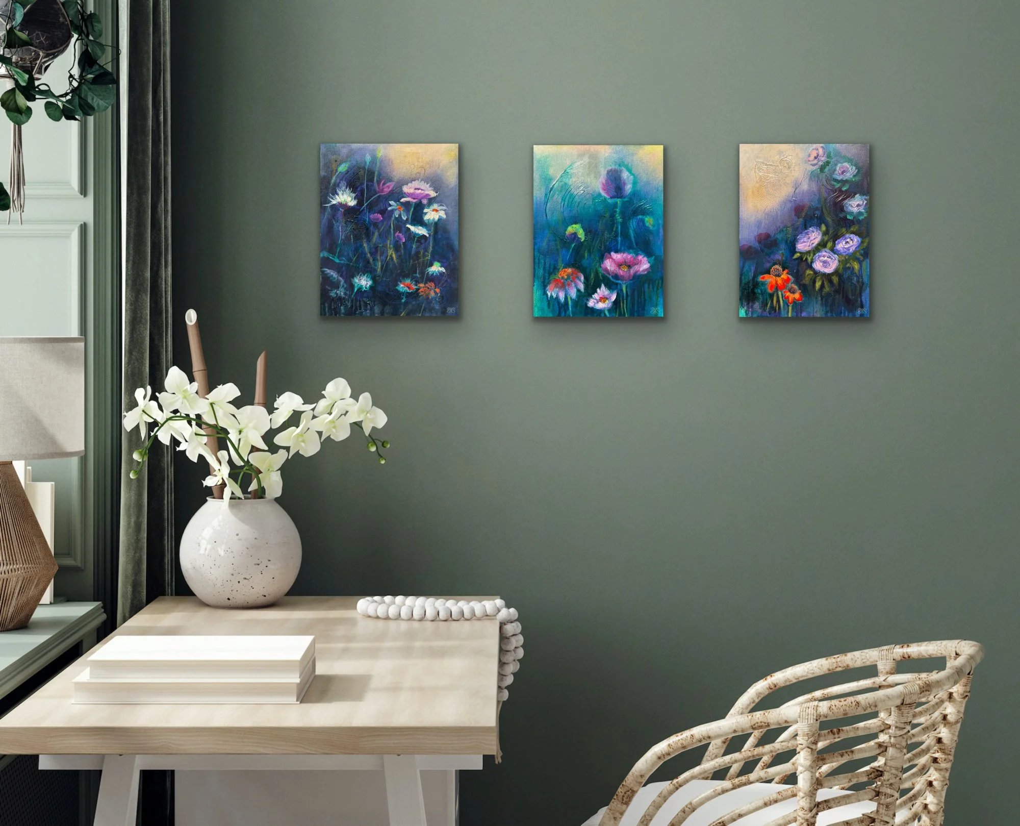 Interior of a room displaying three colorful floral paintings on a green wall, with a white vase holding white orchids on a light-colored wooden table, and a straw chair with curved design in the foreground.