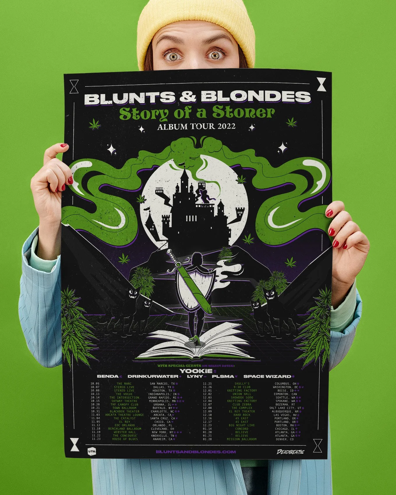 A person holding a concert poster for Blunt & Blondes' 2022 tour, featuring a castle, a knight-like figure, and green smoky patterns, against a green background.