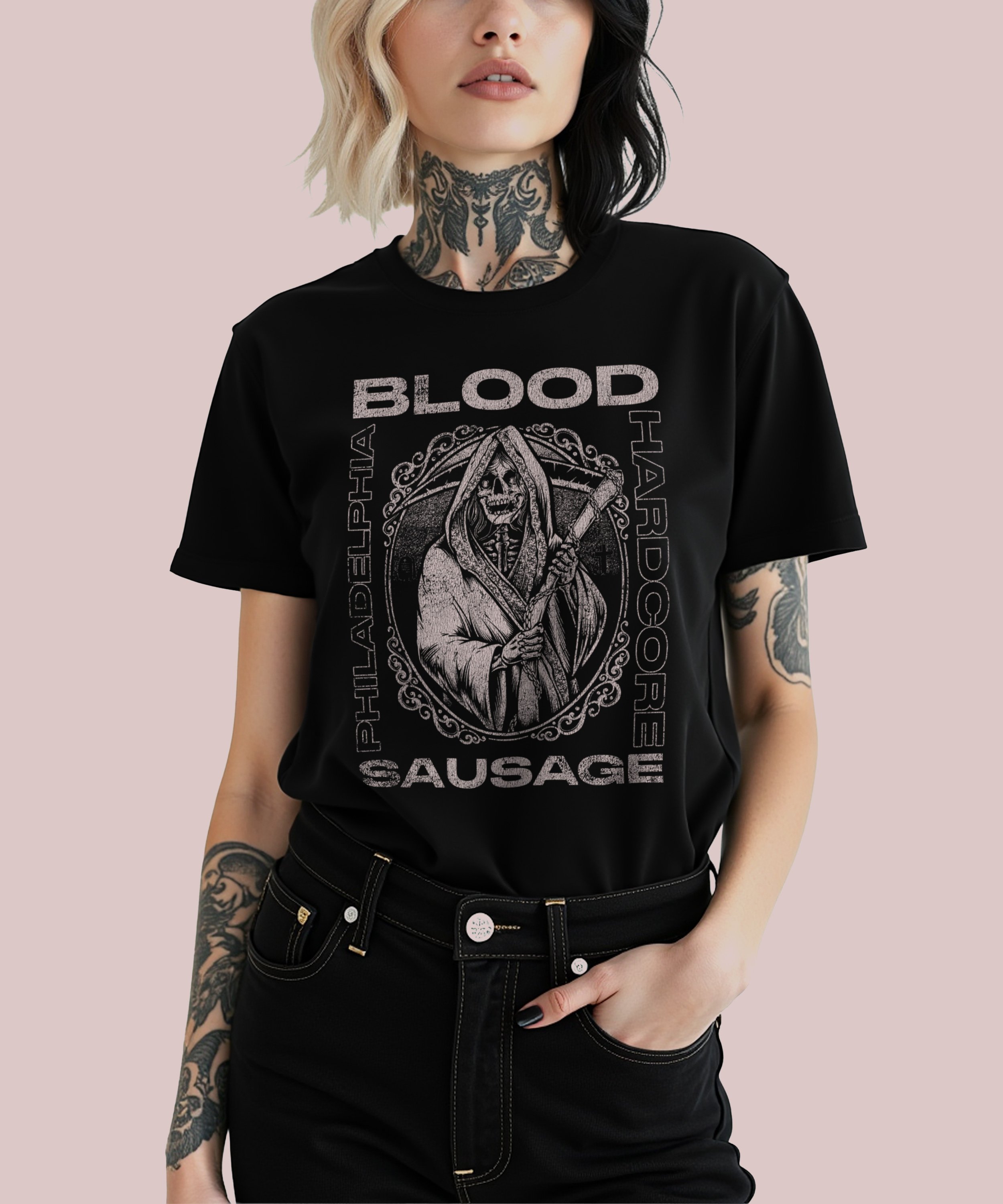 A woman wearing a black T-shirt with a graphic design of a Grim Reaper and text referencing blood, Philadelphia, Holocaust, and sausage. She has black and blonde hair, tattoos on her neck and arms, and is standing against a light pink background.