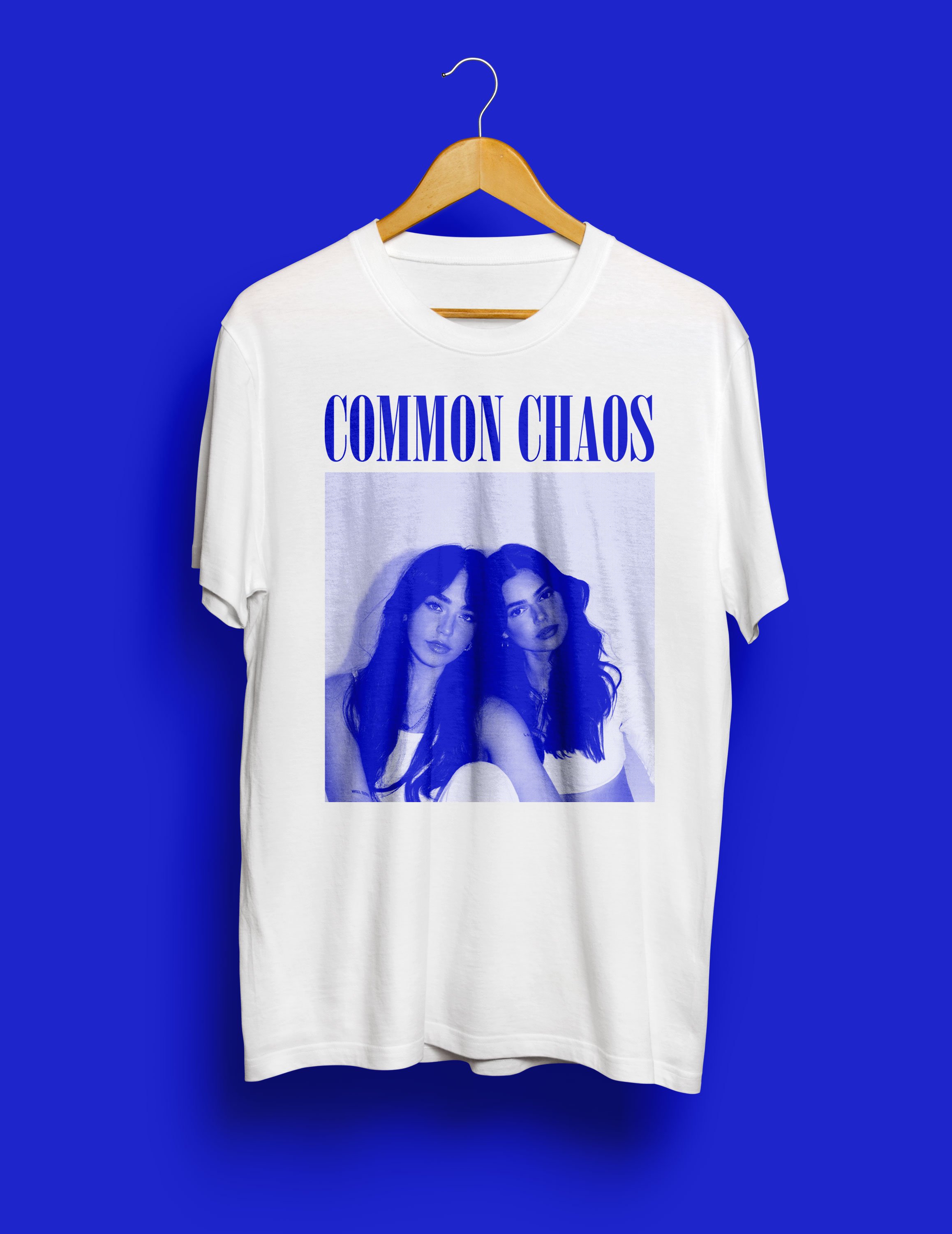 White T-shirt with a black and white photo of two women and the words "COMMON CHAOS" in blue, hanging on a wooden hanger against a blue background.