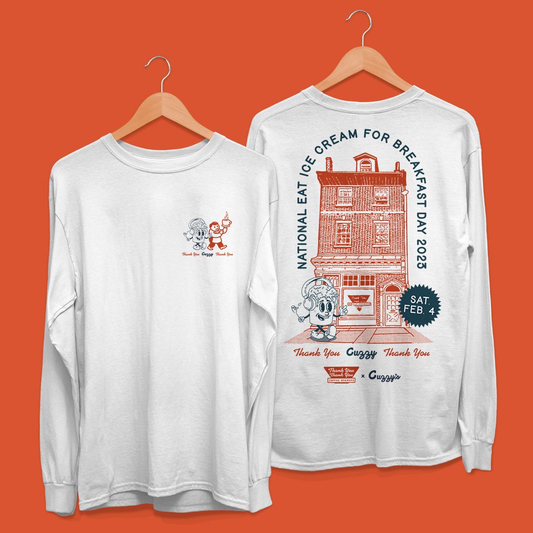 Two white long-sleeve shirts hanging on wooden hangers against an orange background. The shirt on the right features a large graphic of a building with the text "National Eat Ice Cream for Breakfast Day 2023" and a cartoon character with headphones i