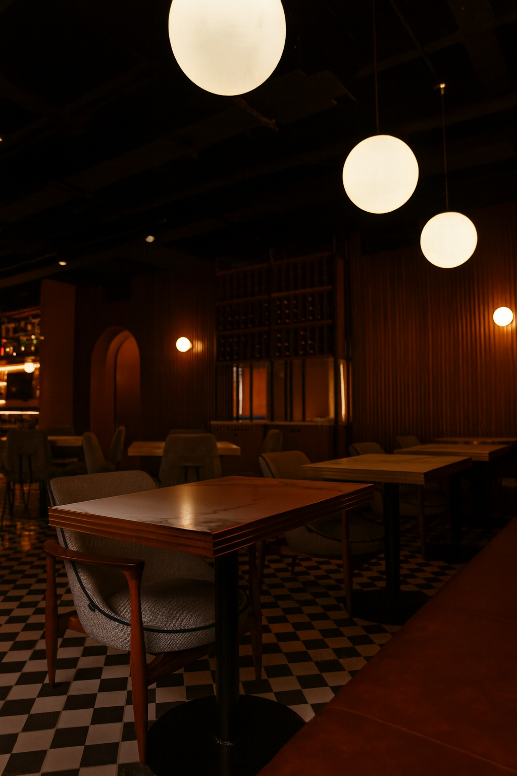 Interior of a dimly lit restaurant with hanging round pendant lights and a checkered floor.