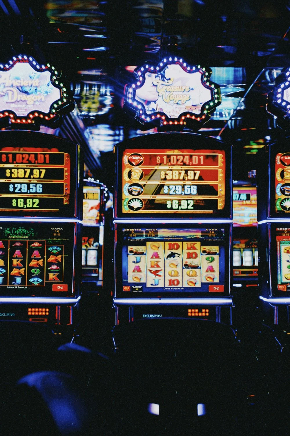 Three slot machines with bright lights and digital displays in a casino, featuring various game symbols and colorful graphics.