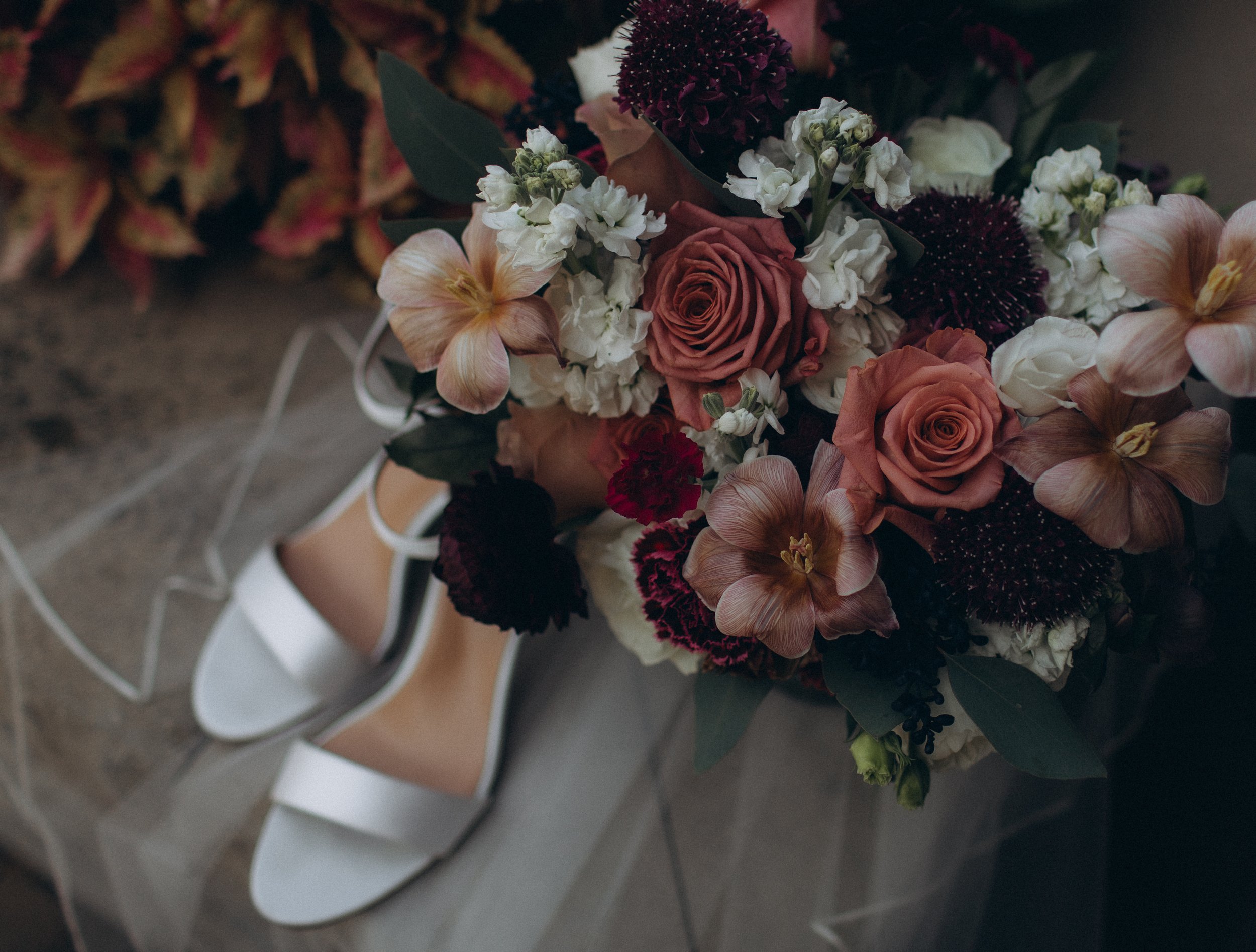 A bouquet of mixed flowers including roses, orchids, and other greenery sitting on a bed with a metallic chair nearby.