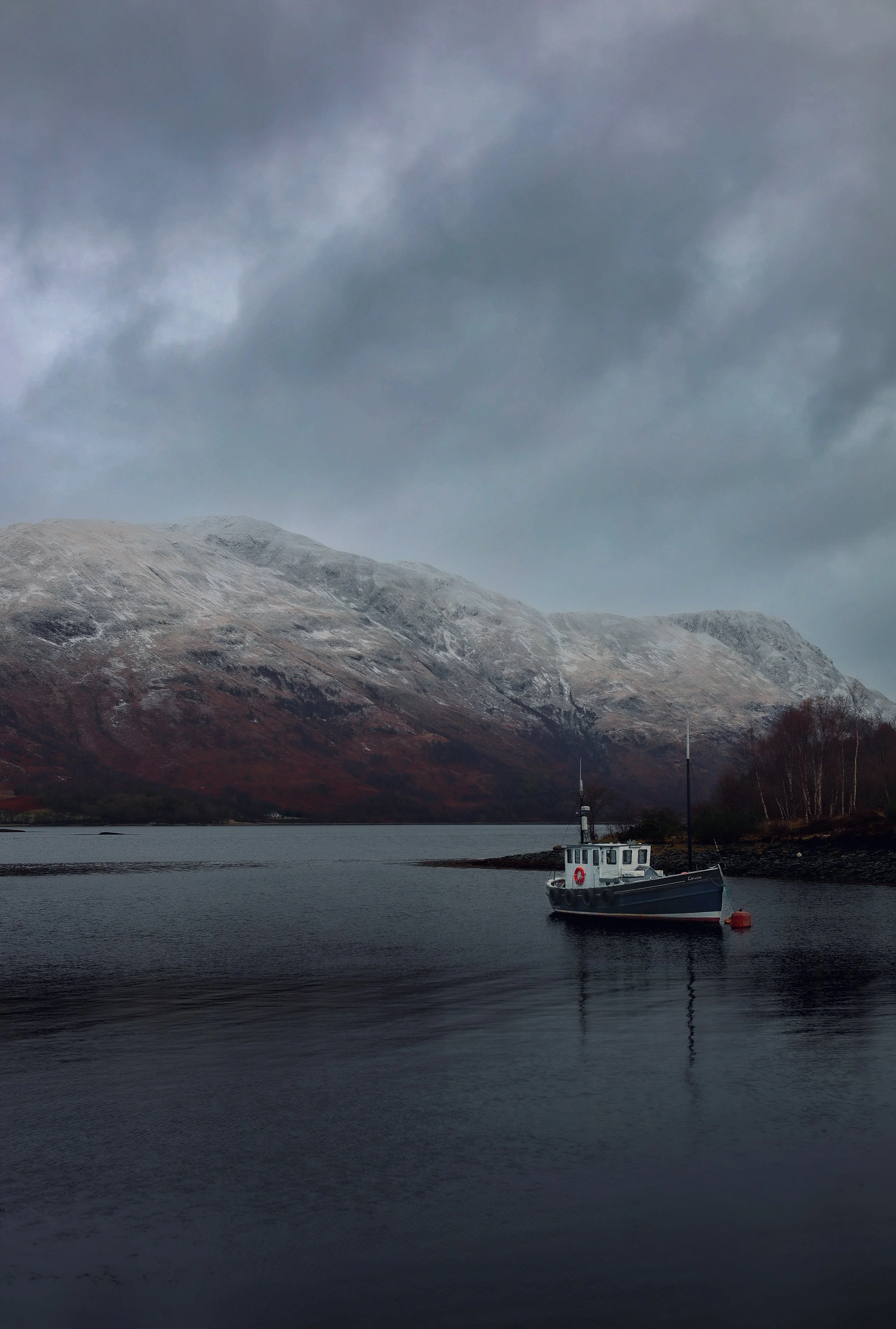 A boat floating on calm water with a mountain range in the background under a cloudy sky.