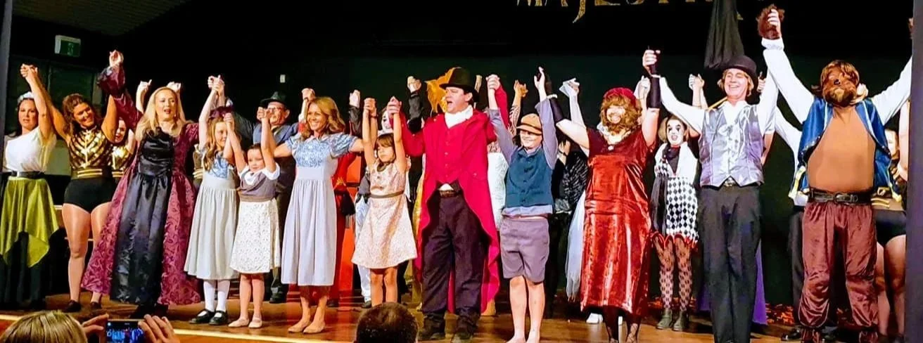 Group of people dressed in costumes on stage, bowing and holding hands in a theatrical performance or play.