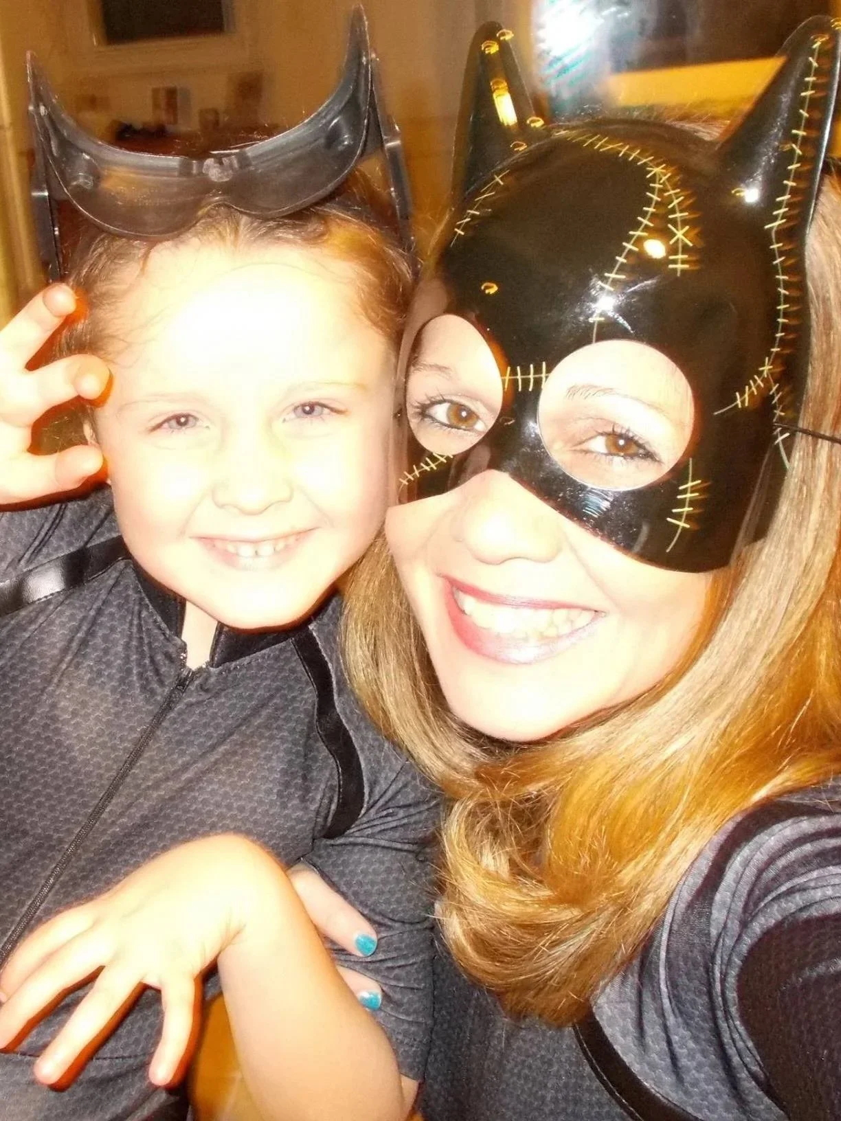 A woman and a young girl dressed up in superhero costumes, wearing masks and smiling for a selfie.