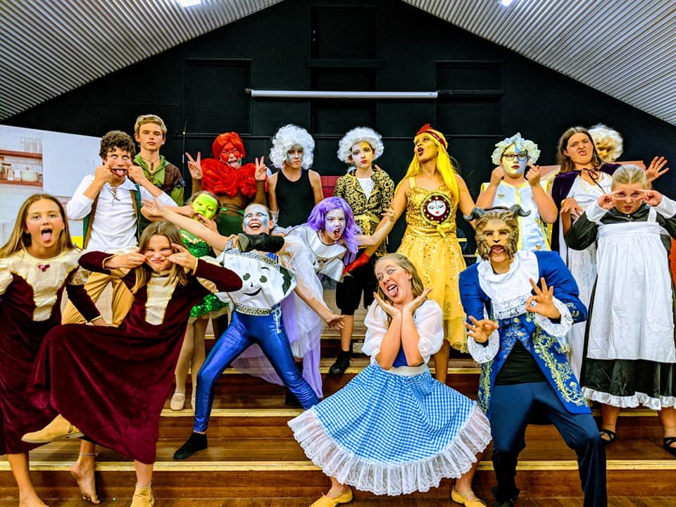 Group of children and adults dressed in costumes as characters from 'Alice in Wonderland' during a stage performance or costume event.