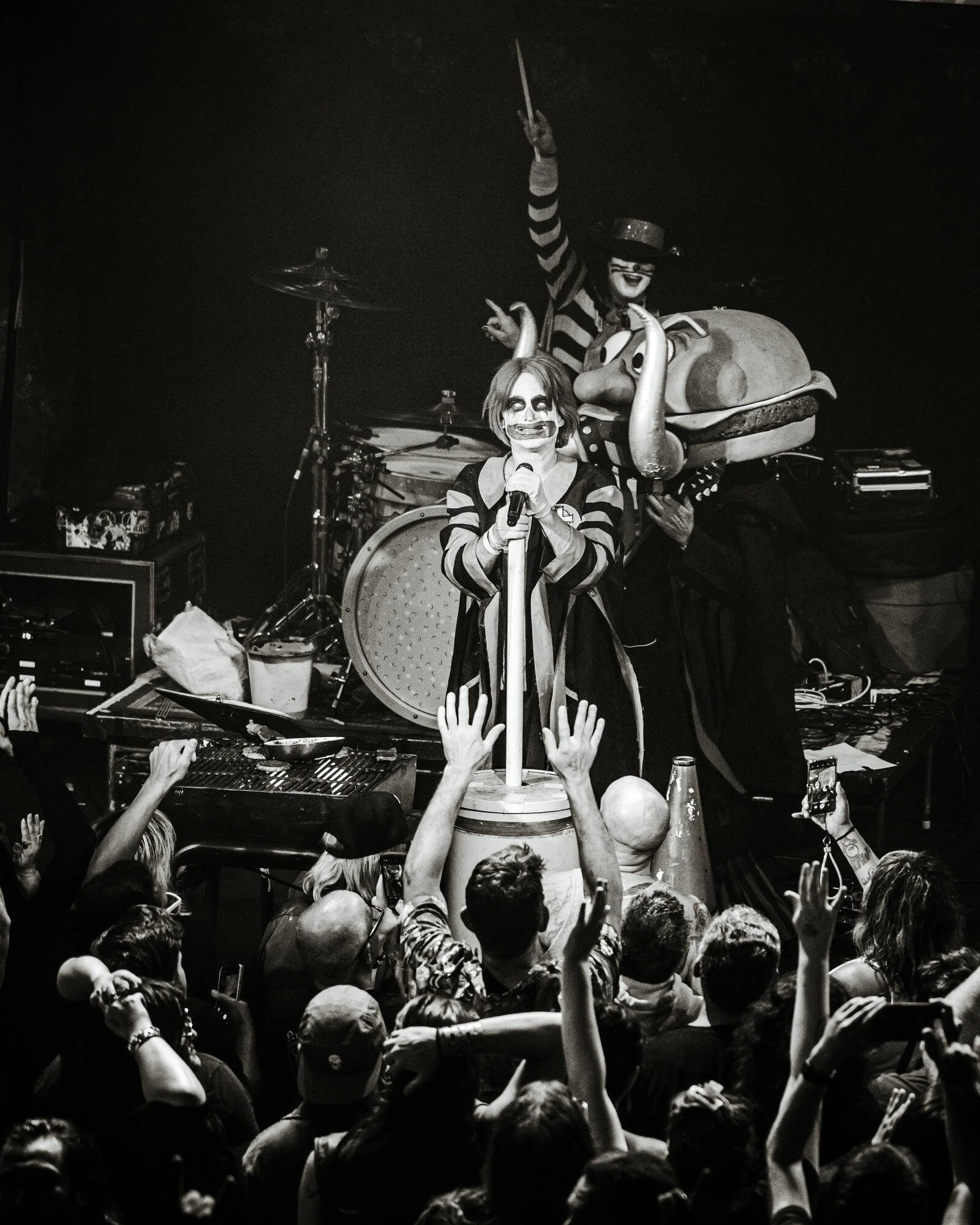 Performers dressed as clowns on stage entertaining a crowd, with hands raised in the audience and racing fans.
