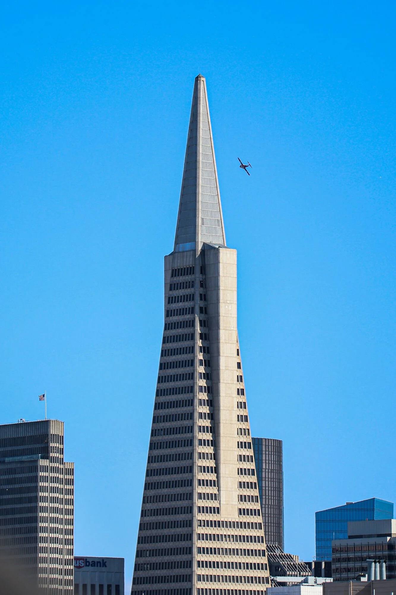 The Transamerica Pyramid, a tall, pointed skyscraper in San Francisco, with a clear blue sky and a helicopter flying nearby.