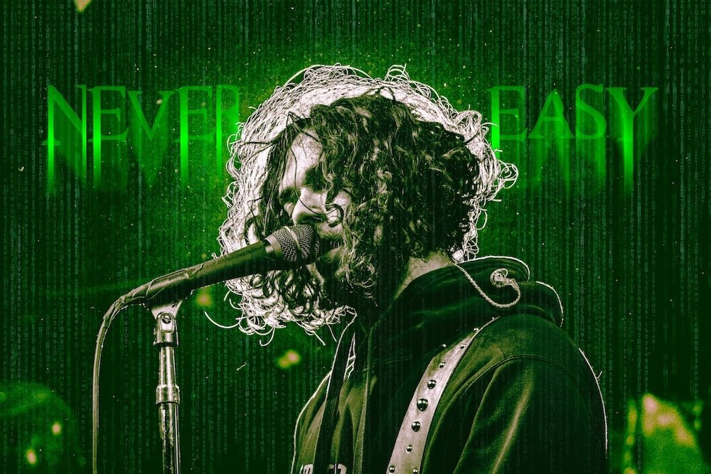 A woman singing into a microphone on stage with green digital effects and the words 'NEVER GIVE UP EASY' glowing behind her.