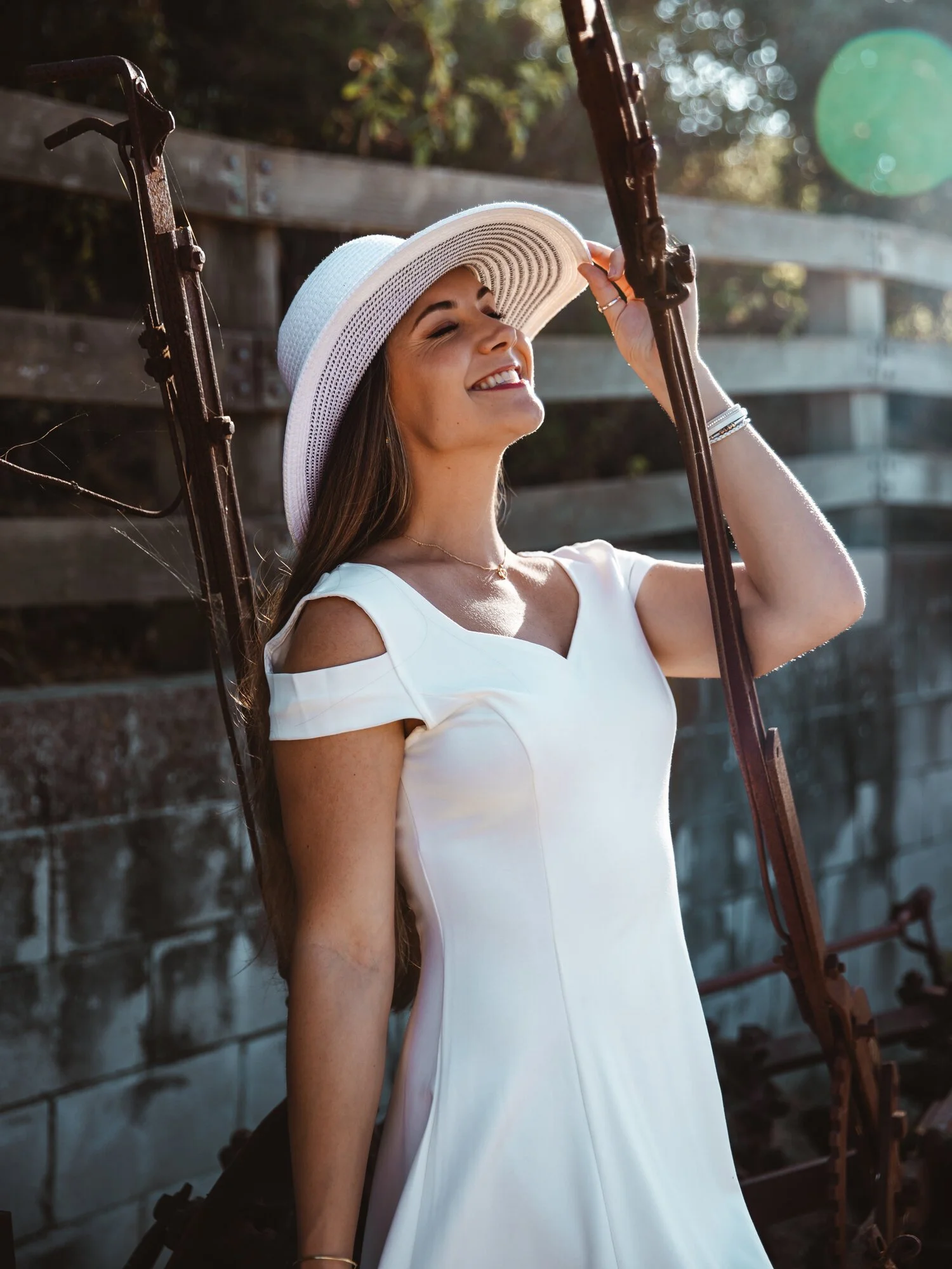A woman wearing a white dress and a wide-brimmed hat smiling outdoors during daytime.