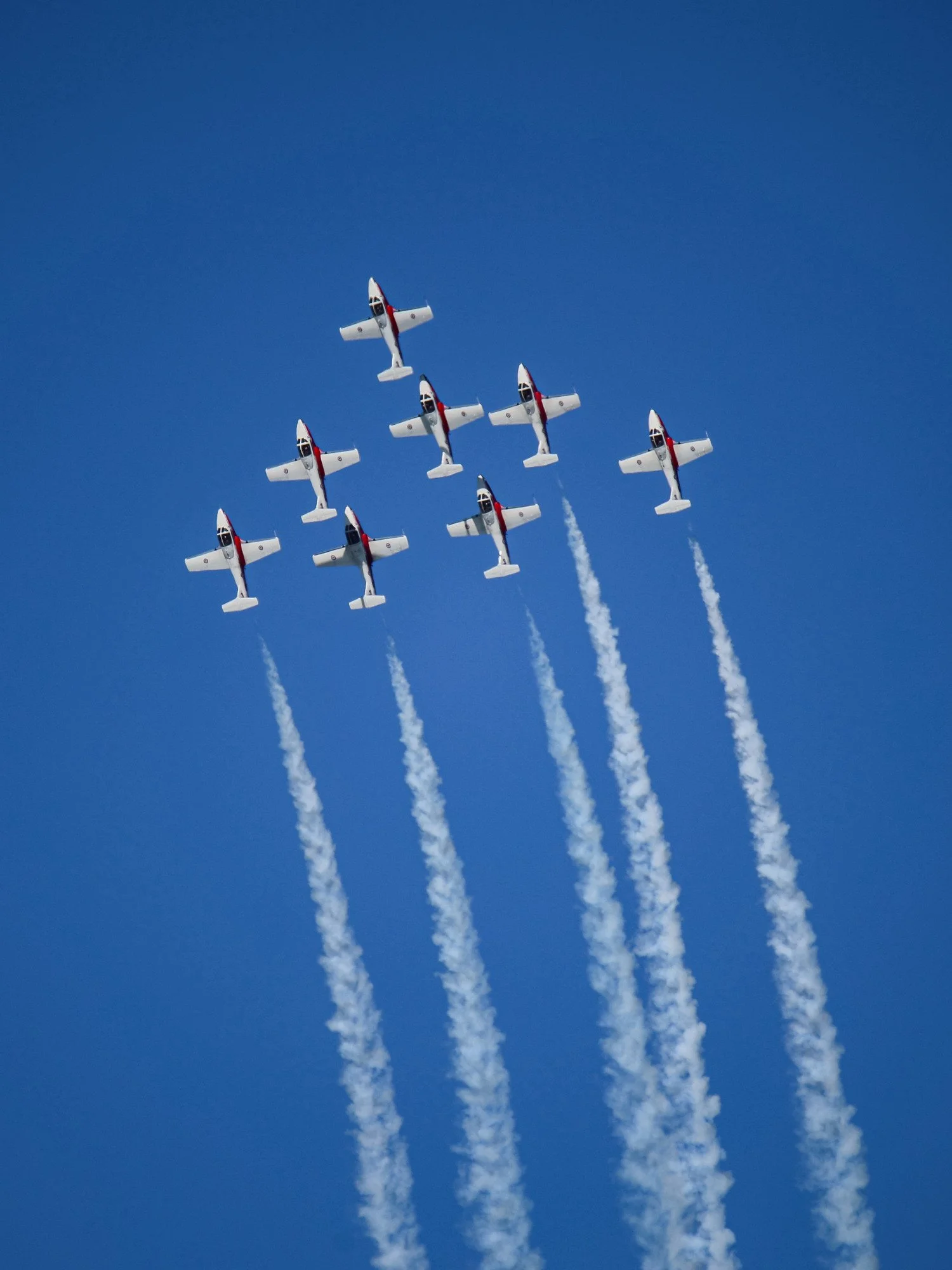 A formation of nine planes flying in clear blue sky, leaving white smoke trails behind them.