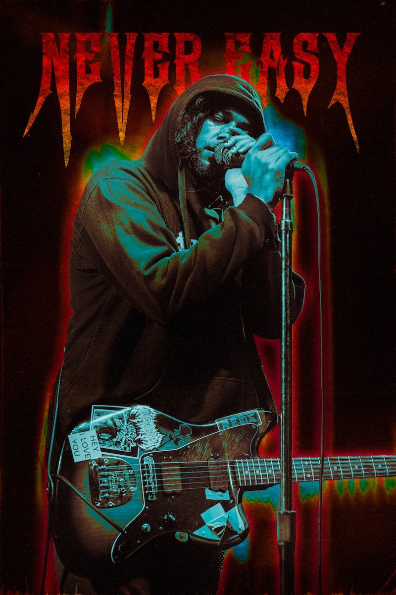 A male musician wearing a hoodie, holding a microphone, and playing an electric guitar decorated with stickers, in front of a dark background with red text that says 'Never Easy'.