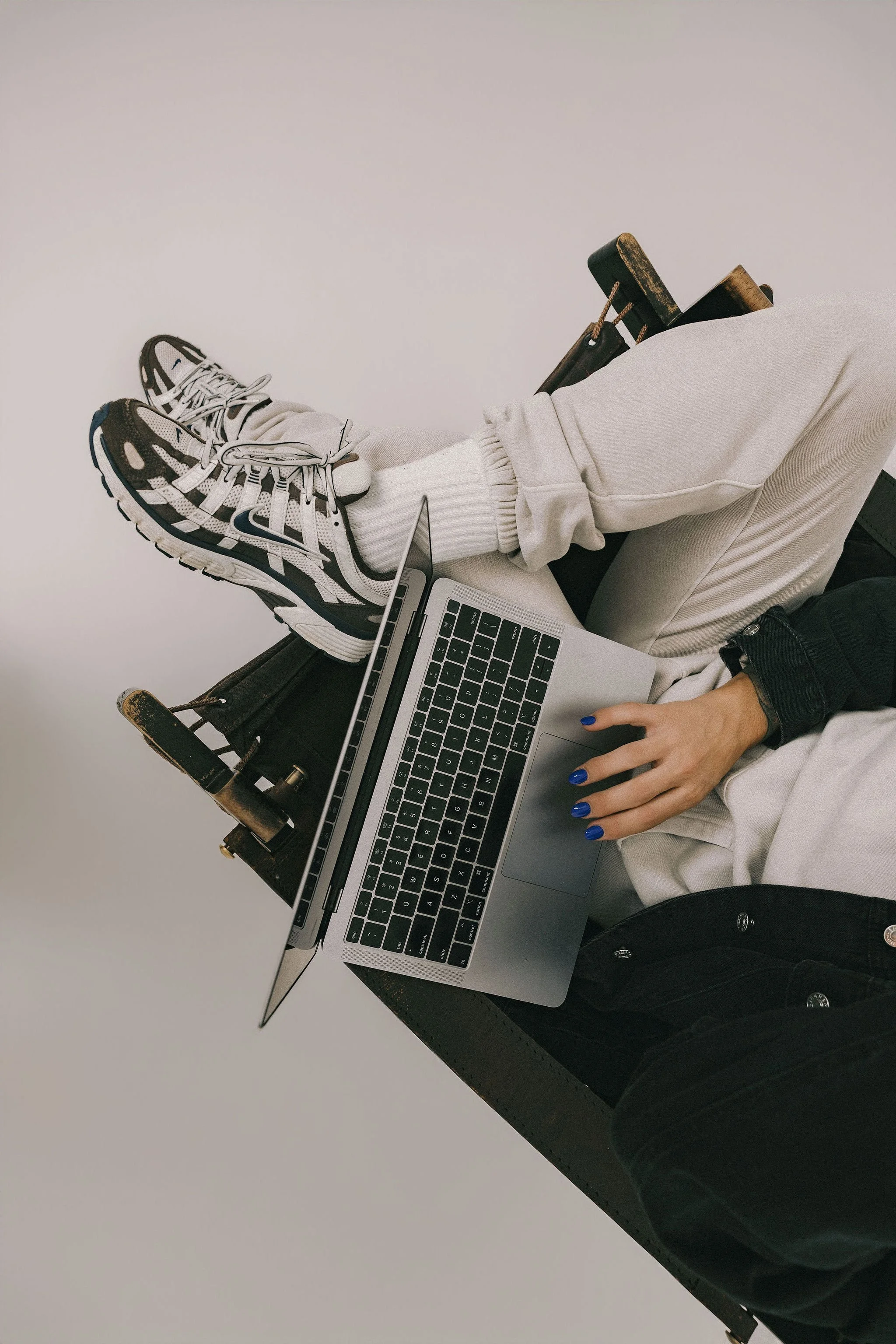 Person sitting cross-legged with sneakers and a laptop, wearing white sweatpants and a black jacket.