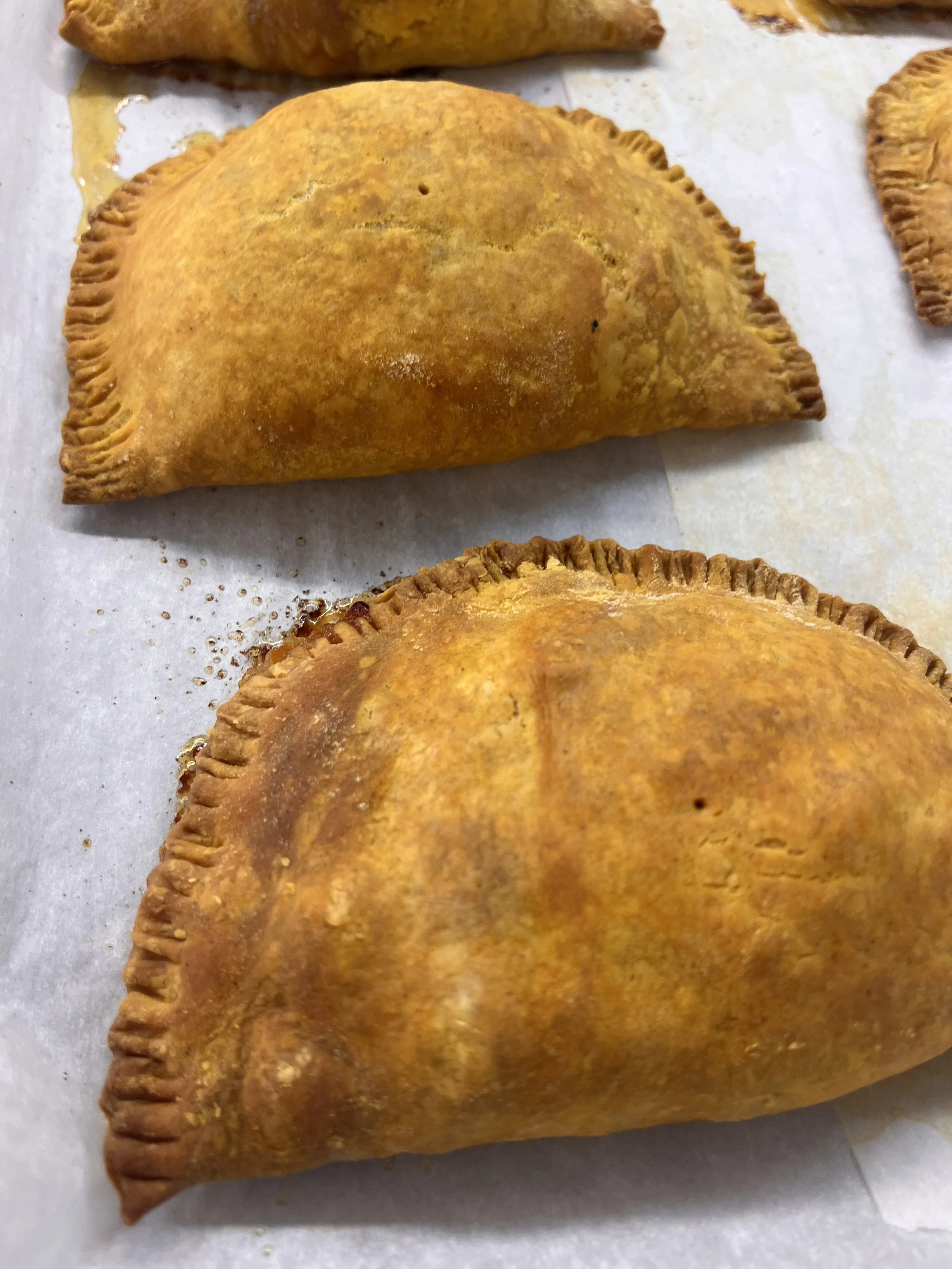 Three baked empanadas with golden-brown crusts resting on parchment paper.