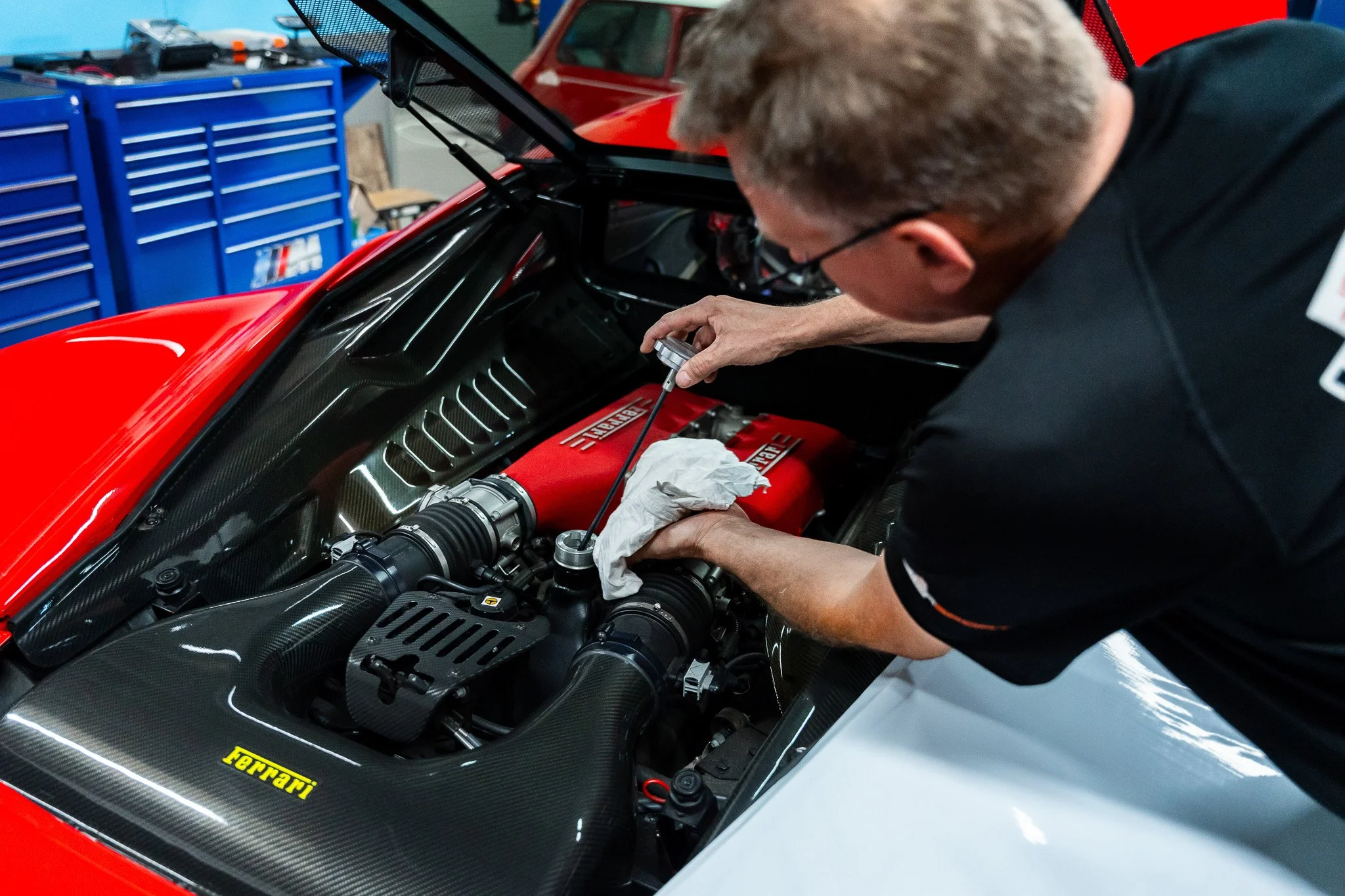 A person working on a red Ferrari race car in a garage, inspecting or repairing the engine with tools.