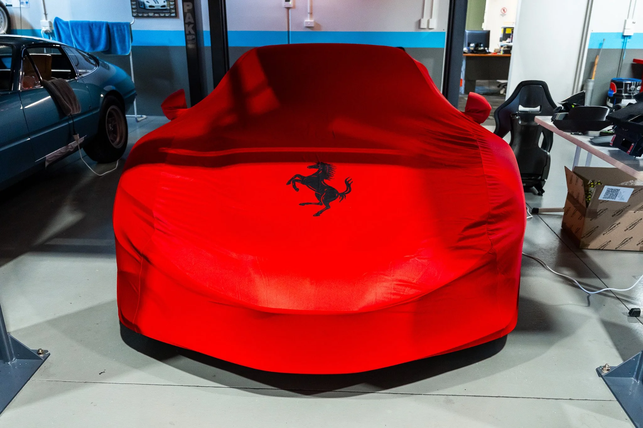 A red cover with the Ferrari logo is covering a sports car inside a workshop or garage.