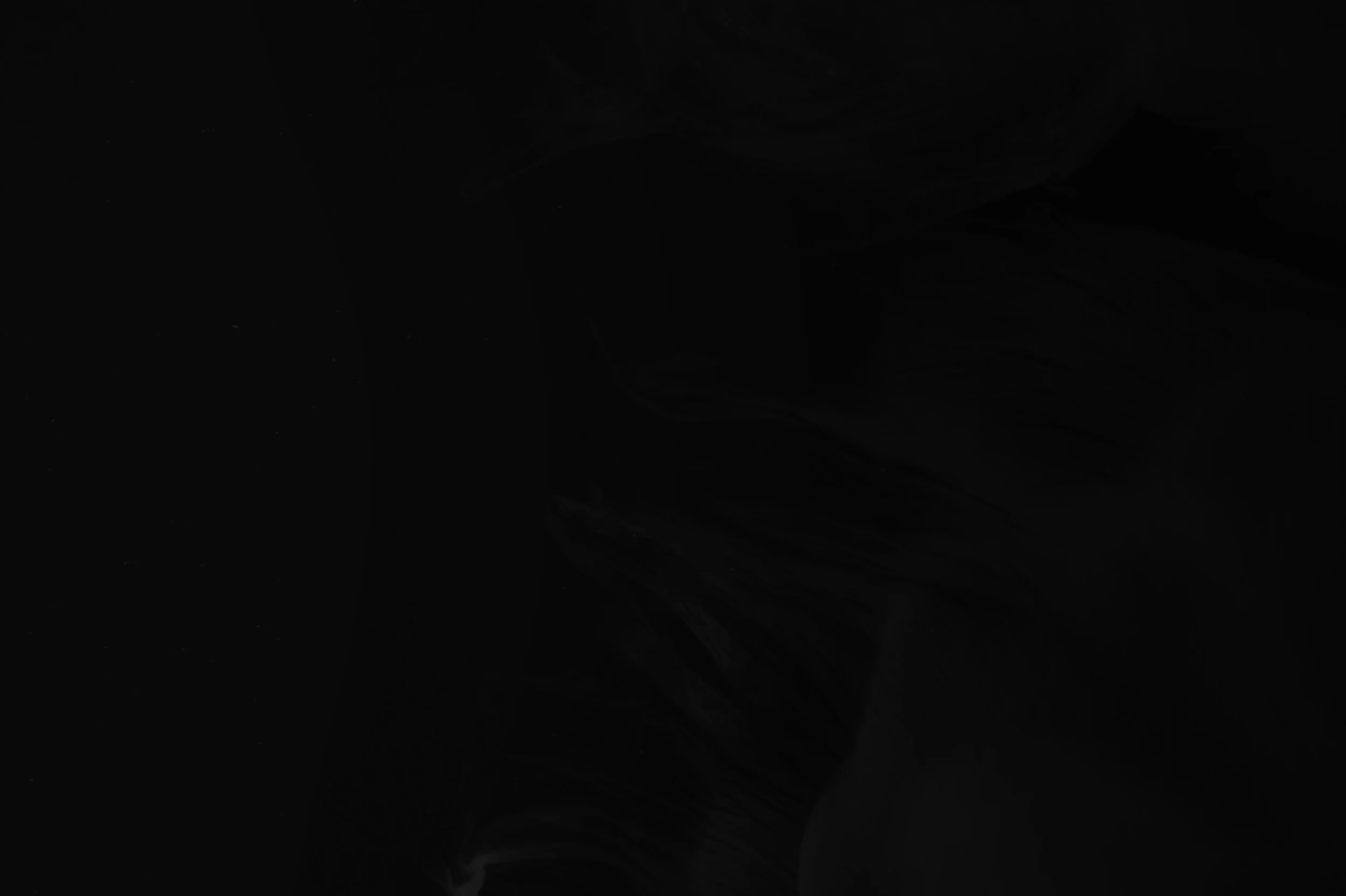 A dark, shadowy landscape with faint, swirling formations in the background, mostly obscured by darkness.