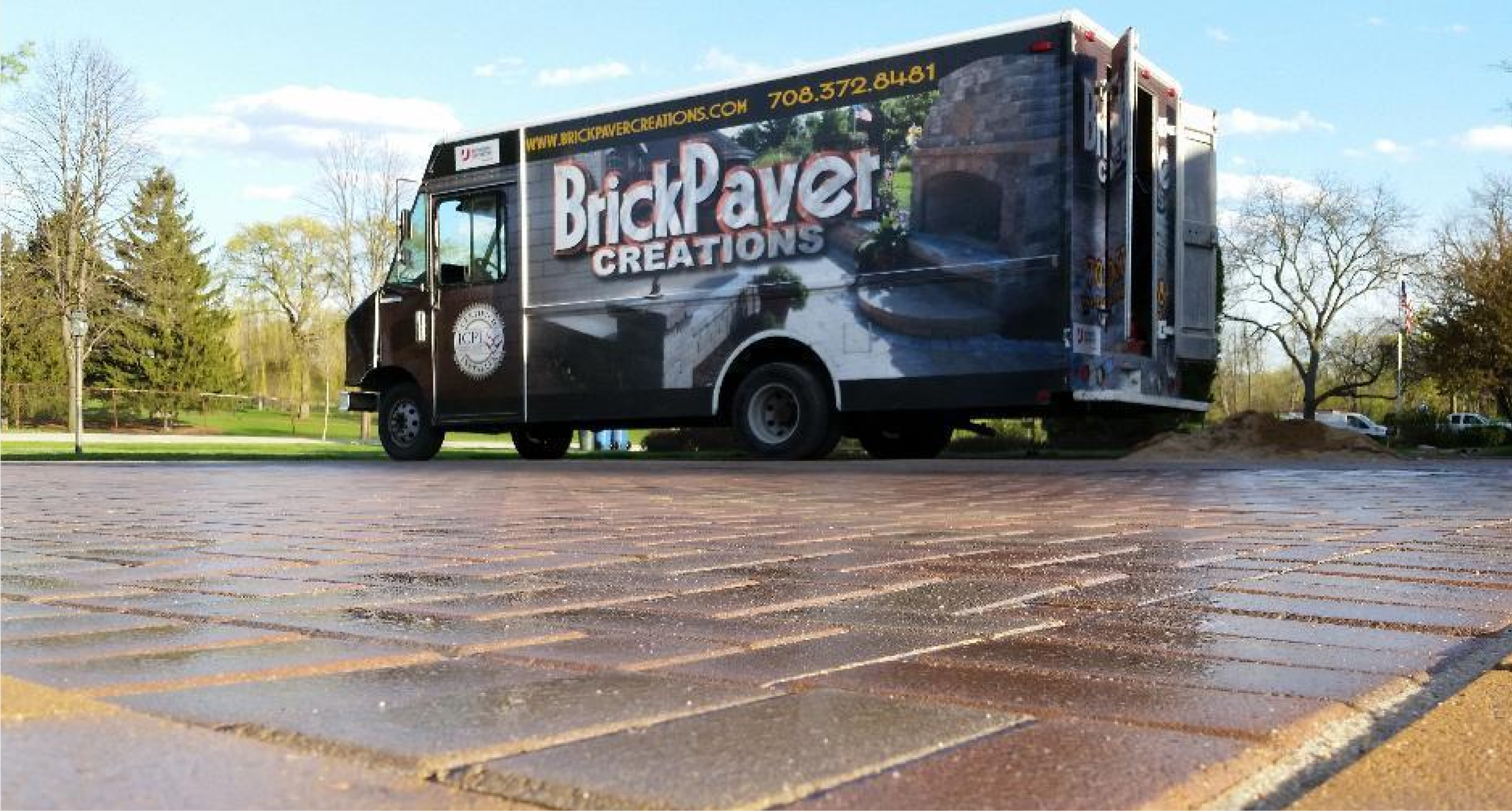 A BrickPaver Creations work truck parked on a wet brick surface, with trees and a partly cloudy sky in the background.