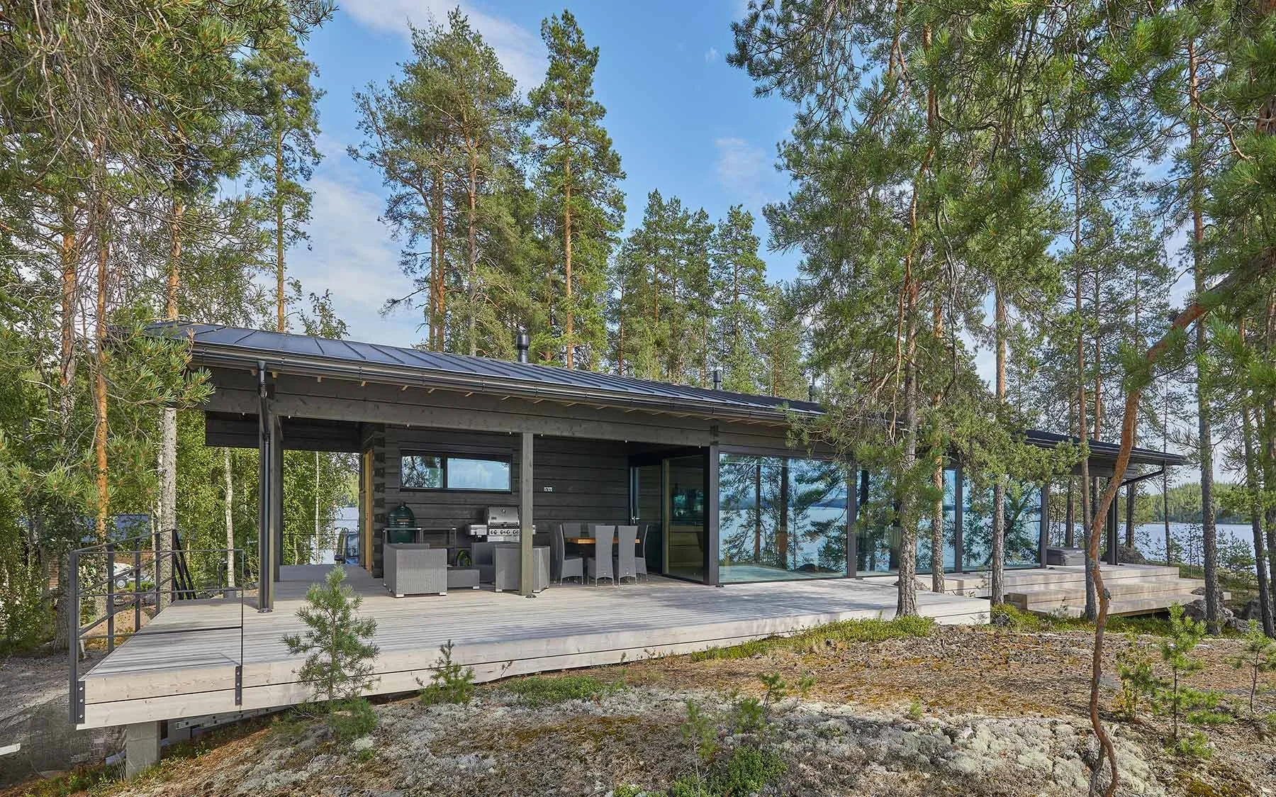 Mustikkainen moderni mökki järven rannalla, ympäröity puille ja luonnon rauhassa.