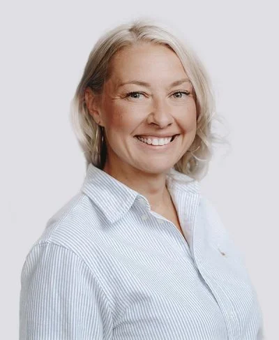 A portrait of a smiling woman with light hair and a charming expression, wearing a white and blue shirt.
