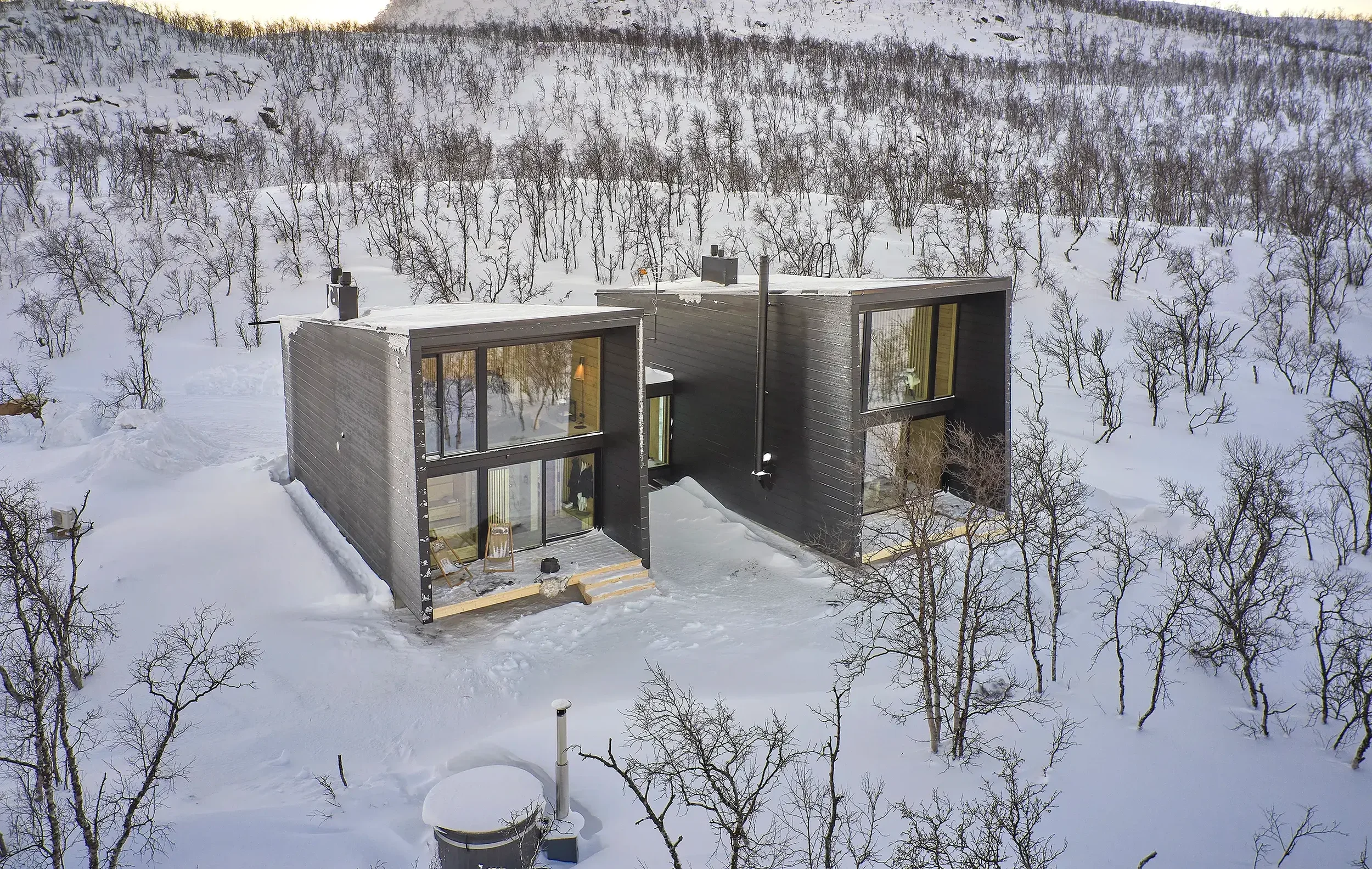 Kaksi modernia mustia taloa lumisessa maisemassa, ympäröi pieniä taloja ja talvisia puita.