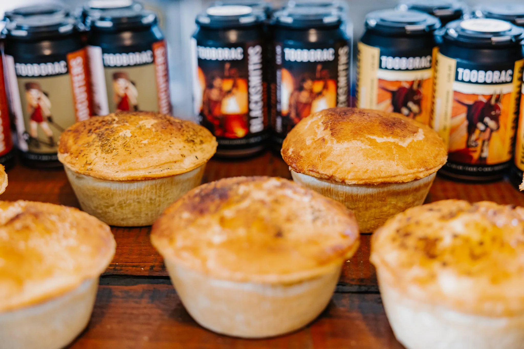 Six freshly baked muffins arranged on a wooden surface with cans of Tooborac tobacco products in the background.