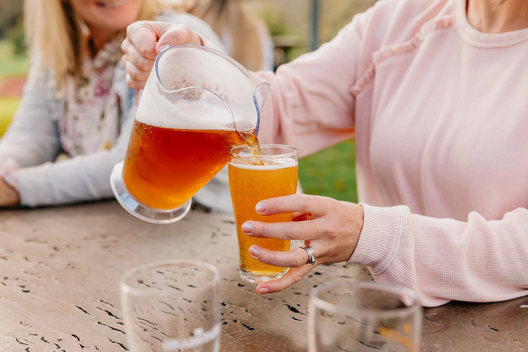 Person pouring beer from a pitcher into a glass at an outdoor gathering.