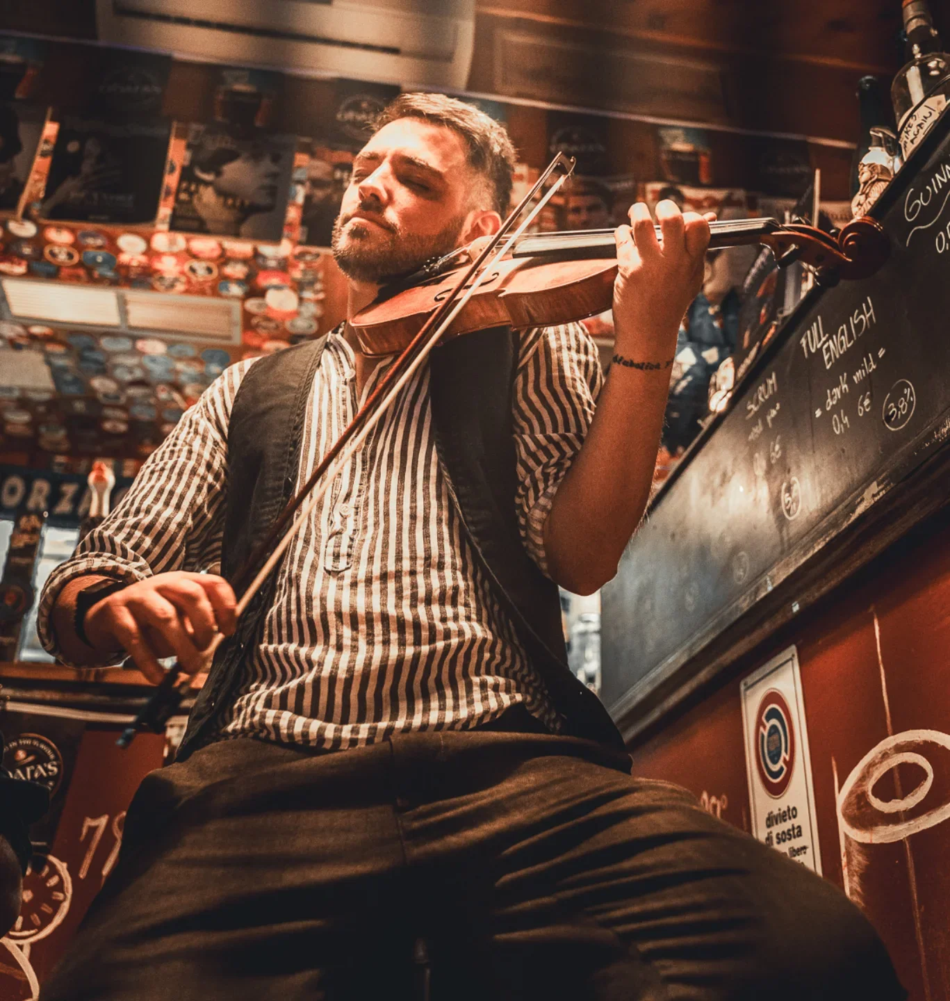 Uomo che suona il violino in un locale con decorazioni e un menu scritto su una lavagna.