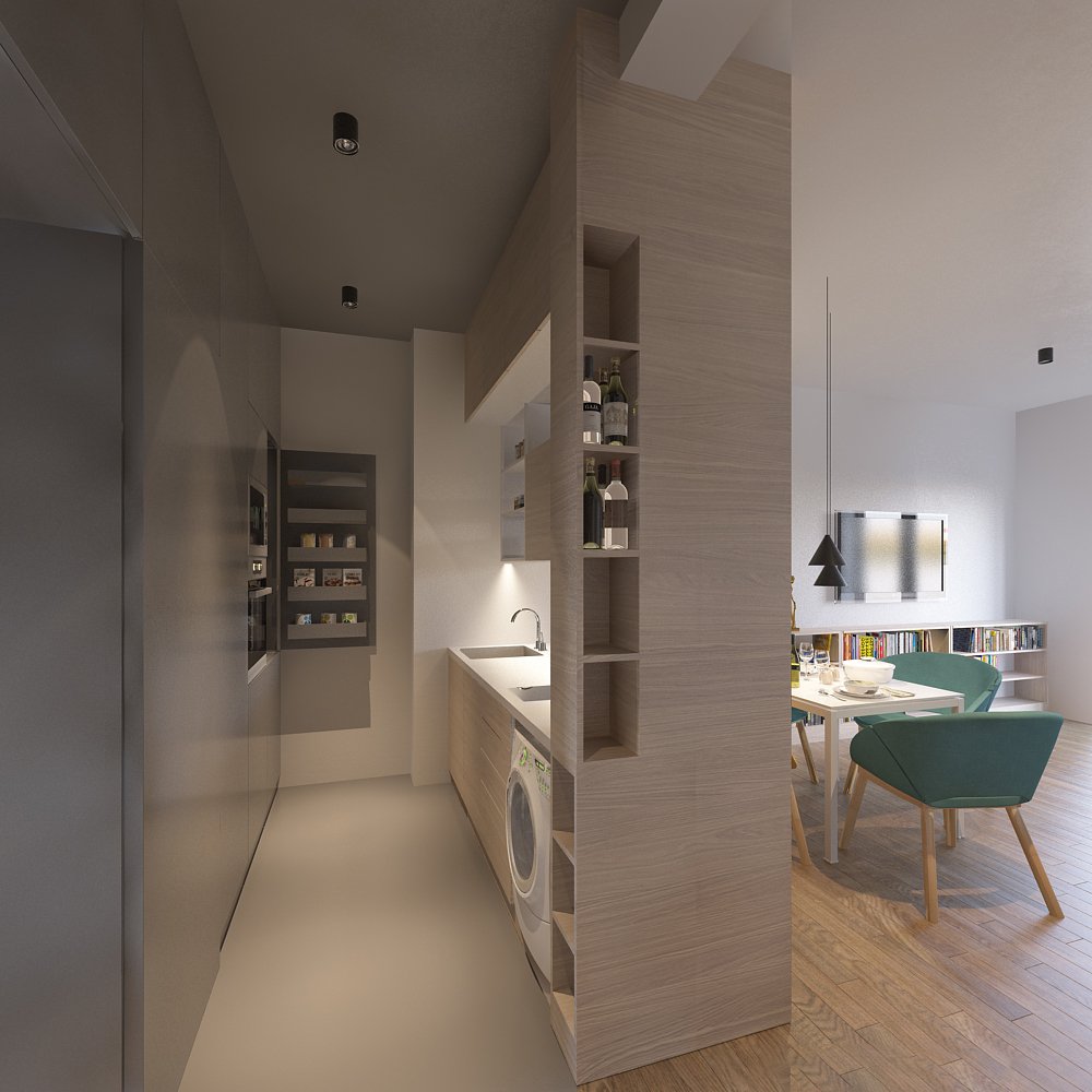 Interior view of a modern apartment showing a small kitchen on the left with built-in appliances and a white countertop, and a dining area on the right with a table, green chairs, and shelving with books.