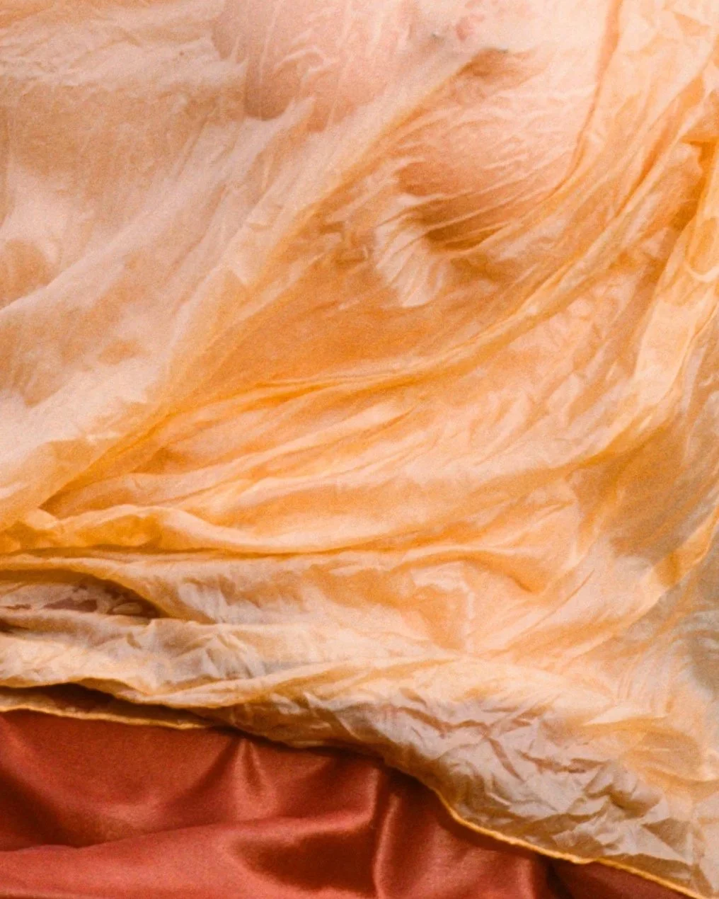 Close-up of a crumpled, beige tissue or paper with a pinkish fabric underneath.