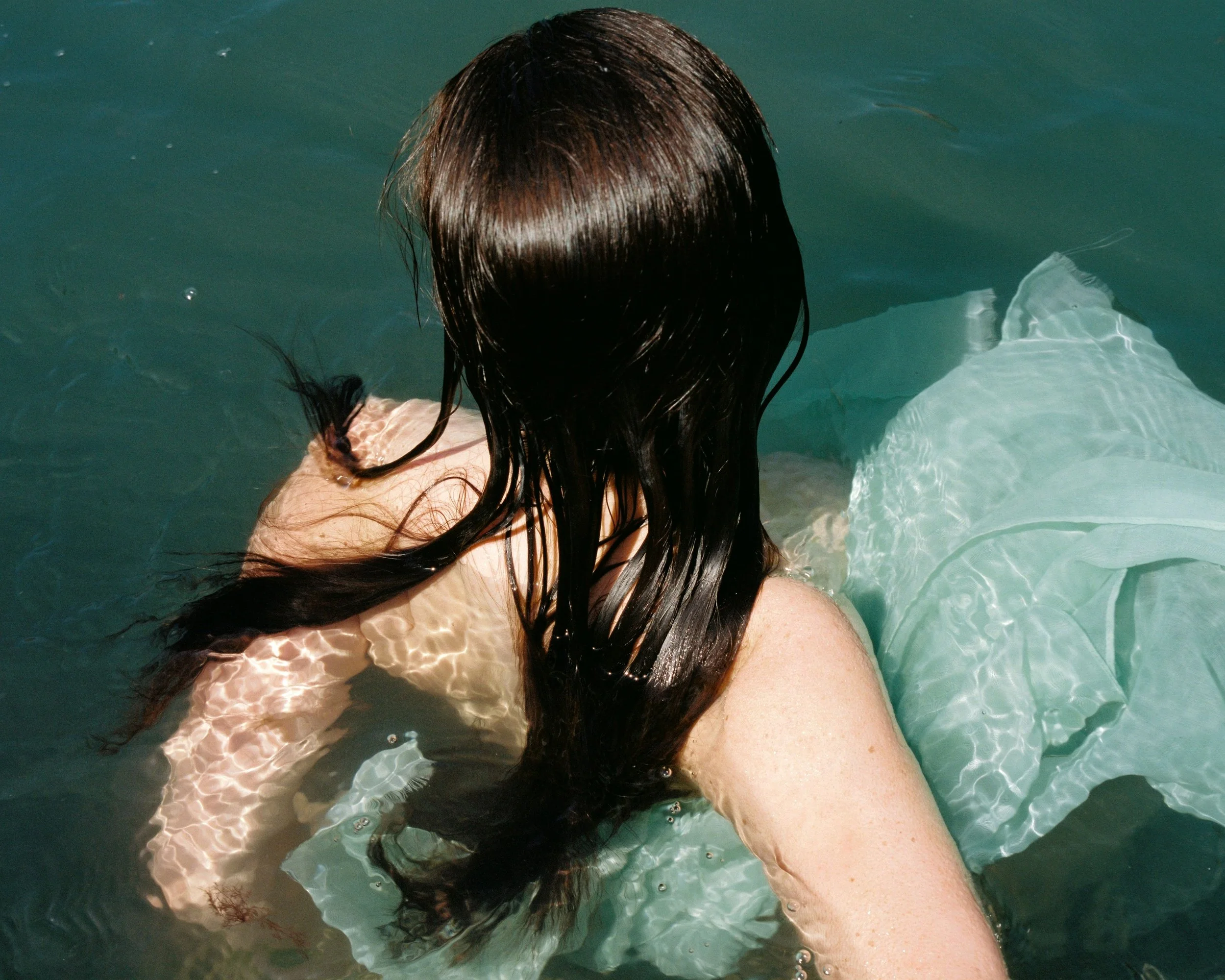 A person with long, dark hair submerged in water, wearing a white dress.