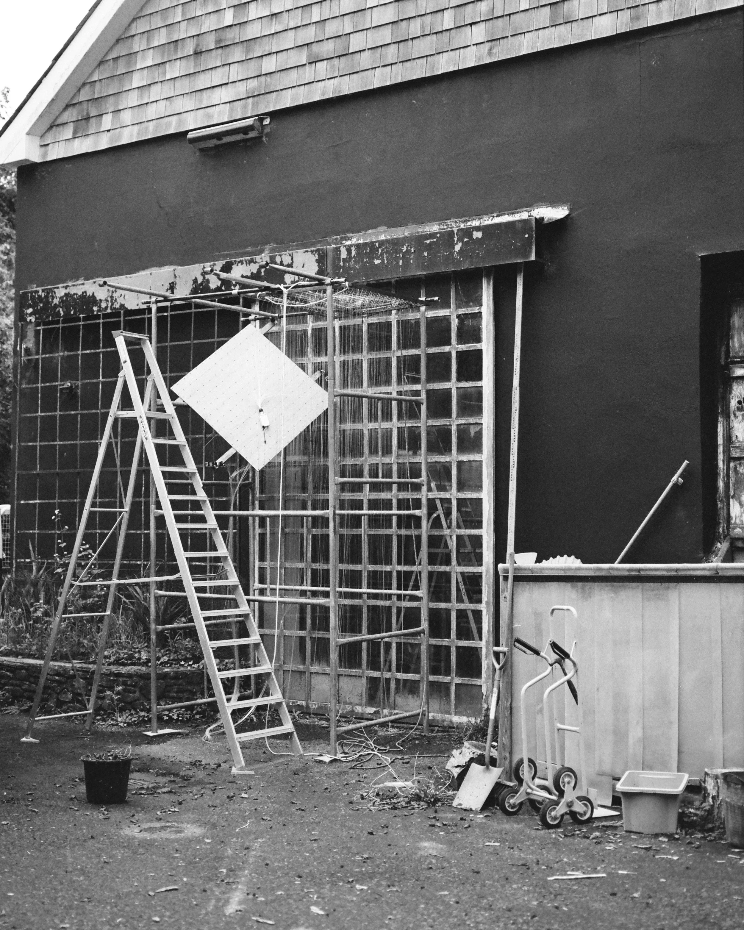 Construction site with scaffolding, a ladder, and tools outside a building with a dark exterior wall.