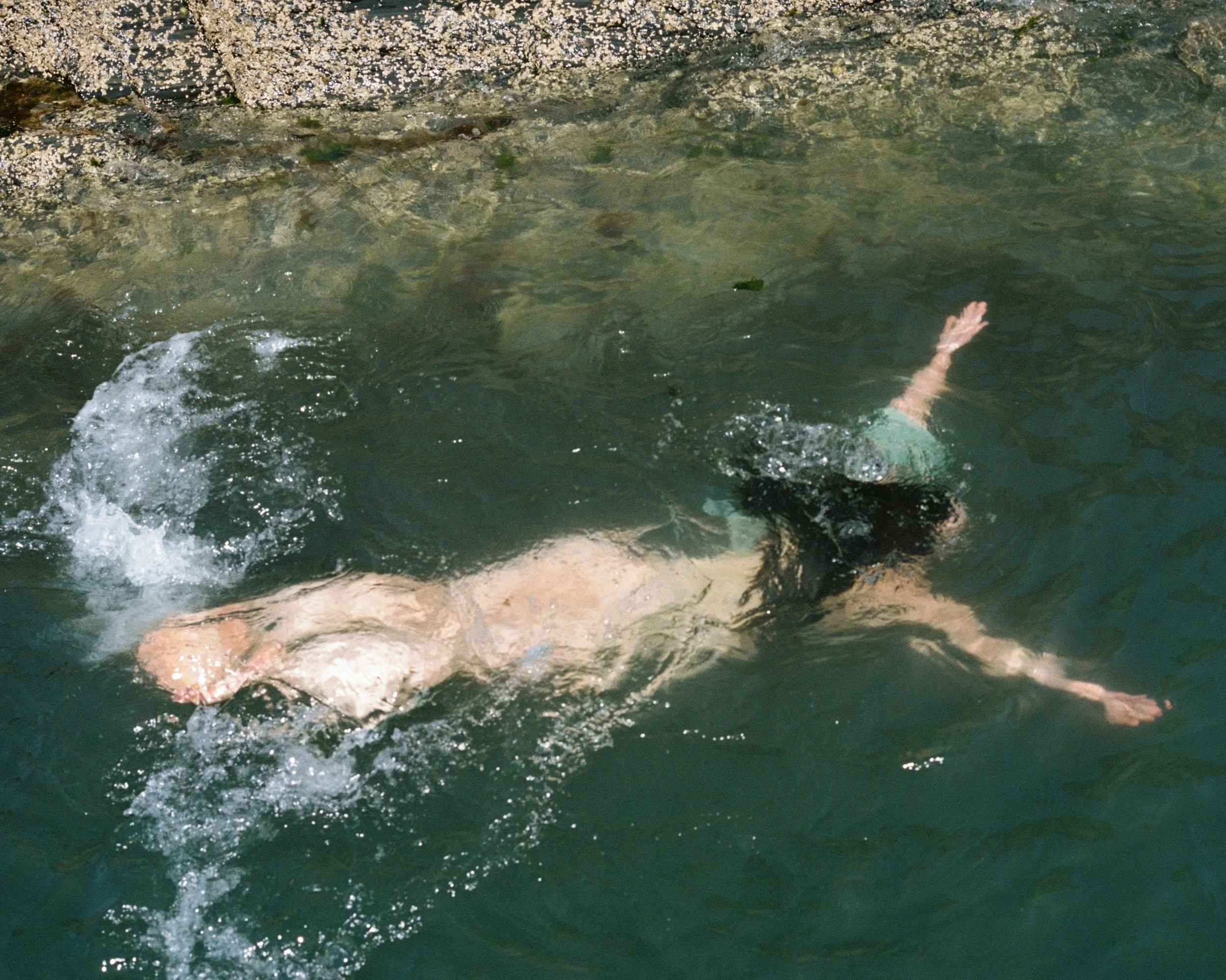 Person swimming in a body of water, with their head submerged and arms extended.