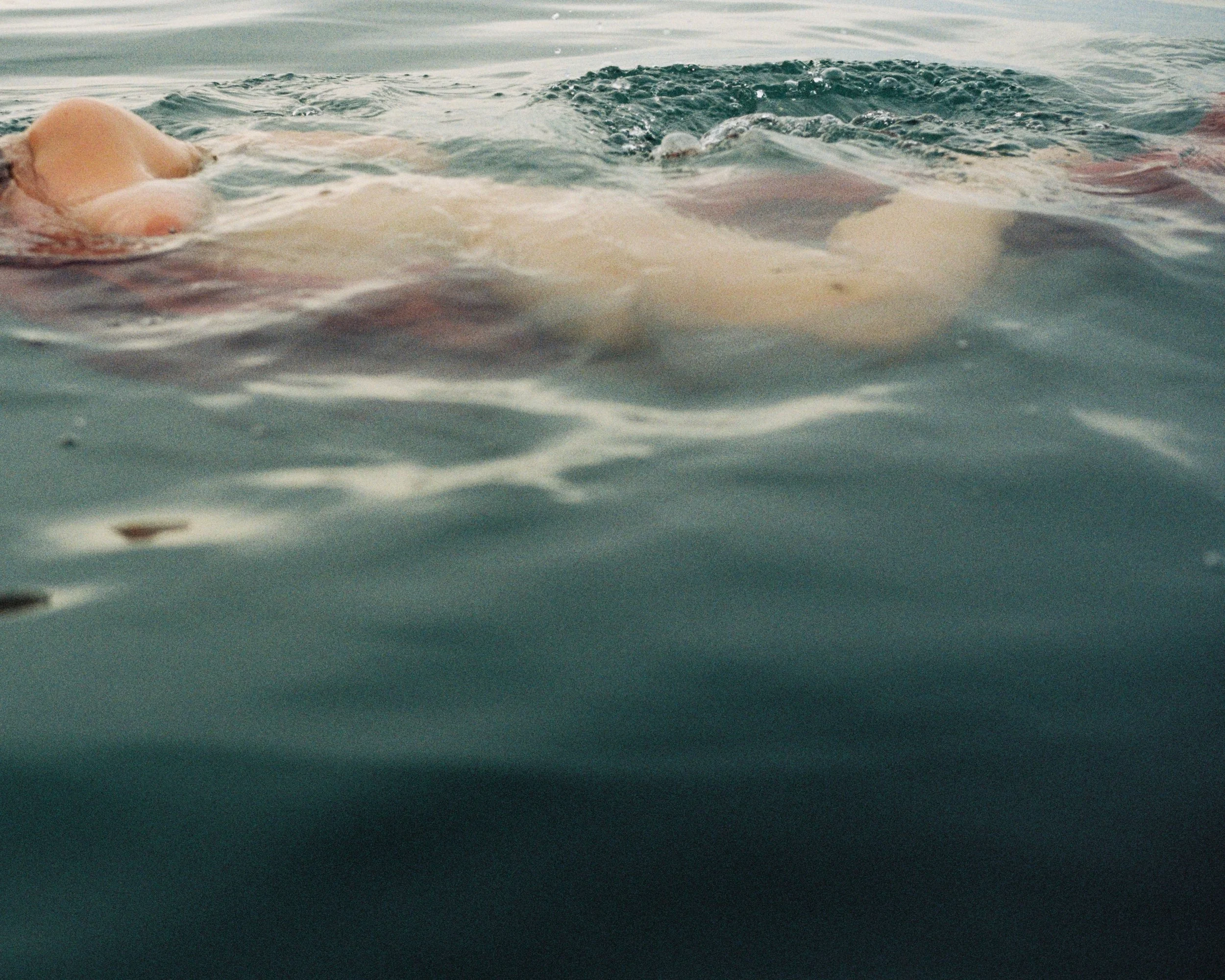 A person floating on their back in a body of water, partially submerged with their head and part of their body visible.