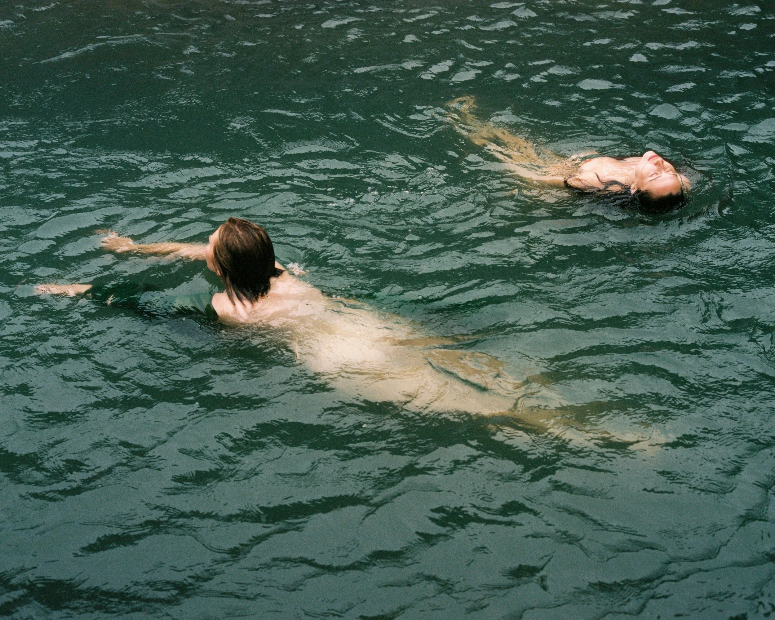 Two people swimming in a body of water, possibly a river or lake.