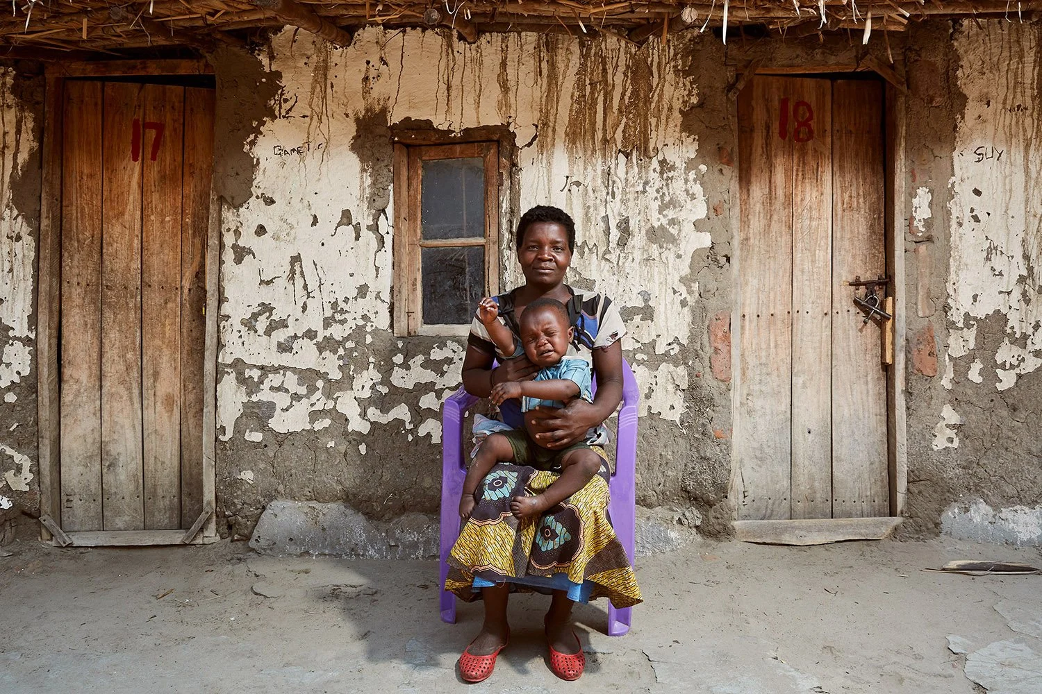 Former fish trader Cathrine sits in front of a building, holding her one-year-old son, Kachulu, Lake Chilwa.