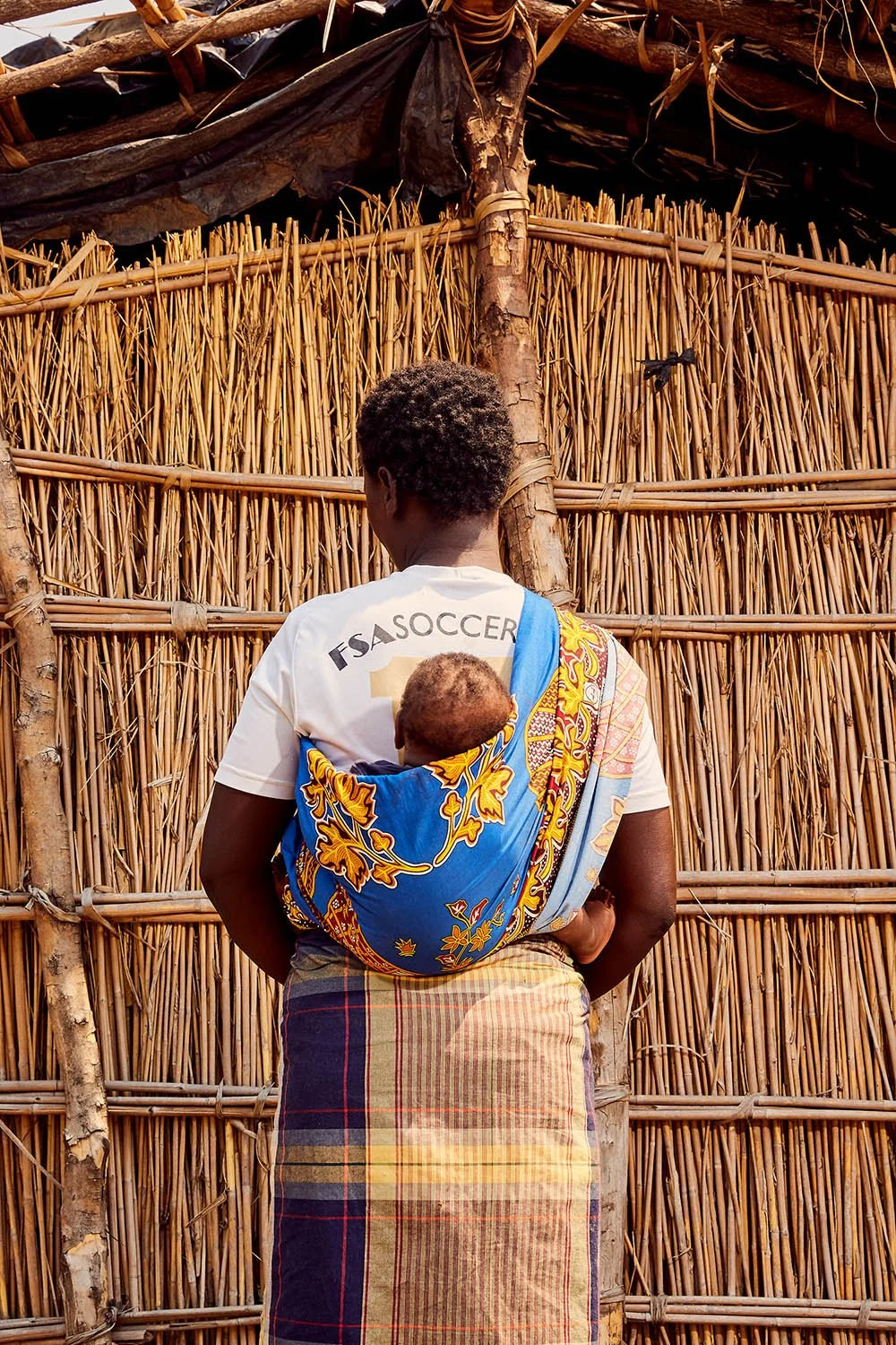 Female Fishtrader stands in front of a reed hut with her son, Elephant Marsh.