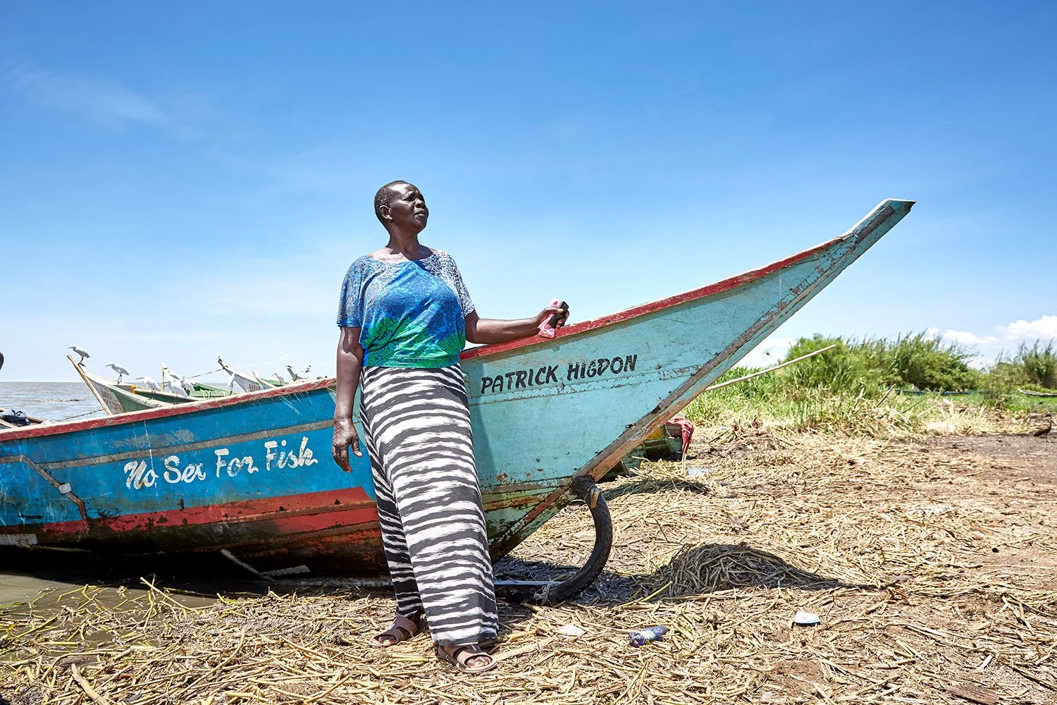 Chairwoman of the No Sex For Fish cooperative, stands by her fishing boat, Nduru Beach, Kisumu, Kenya, 2019.
Patrick Higdon, whose name is on the boat, works for the charity World Connect, which gave the group a grant to provide boats for some of th