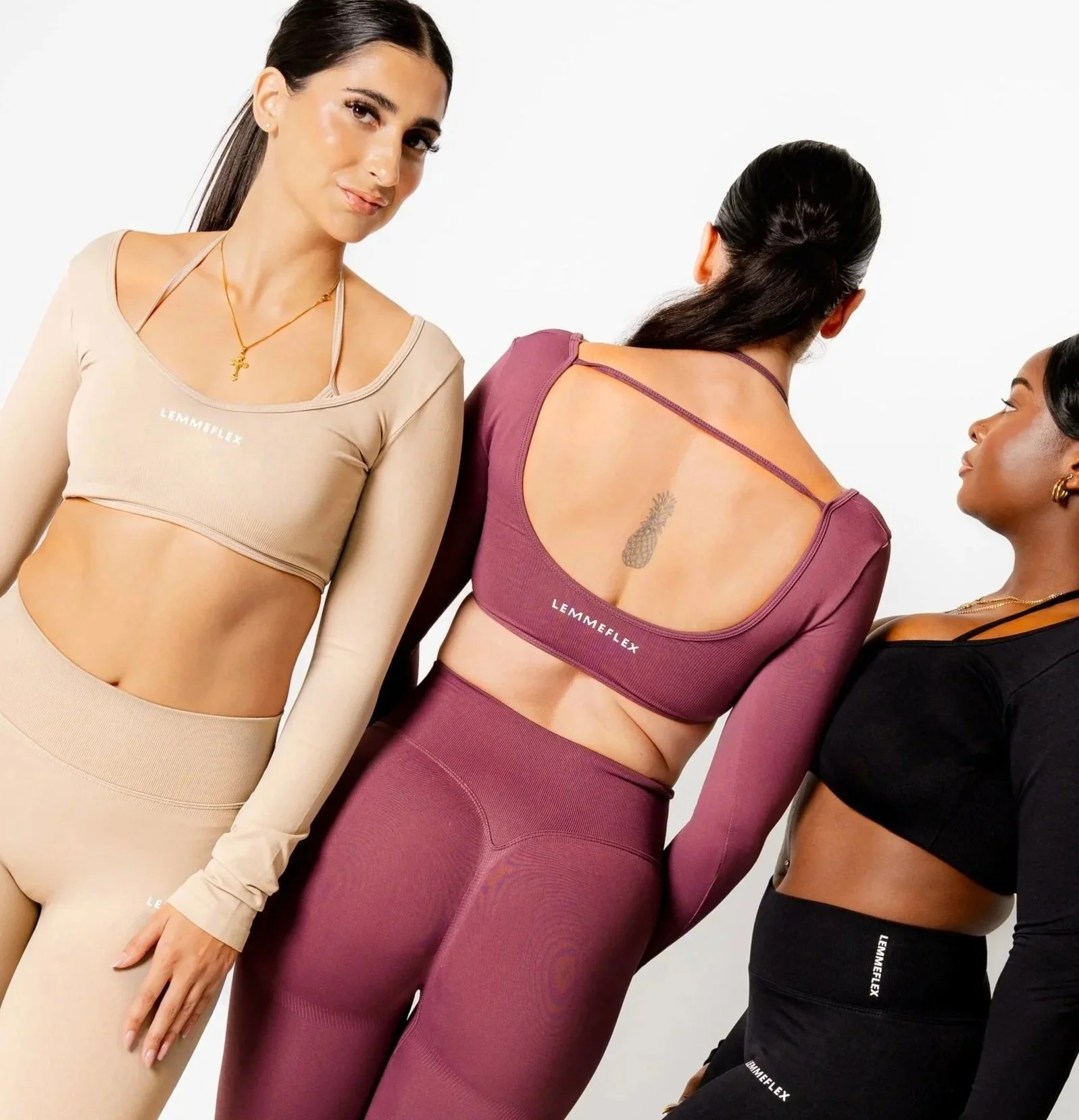 Three women wearing activewear in neutral, mauve, and black, standing side by side against a plain white background, with their torsos and heads visible.