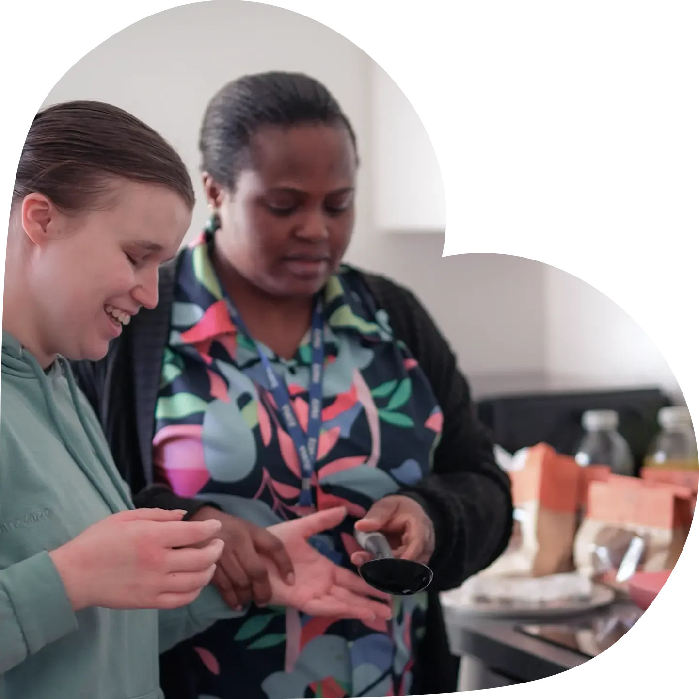 Two women smiling and looking at a phone while standing in a kitchen.