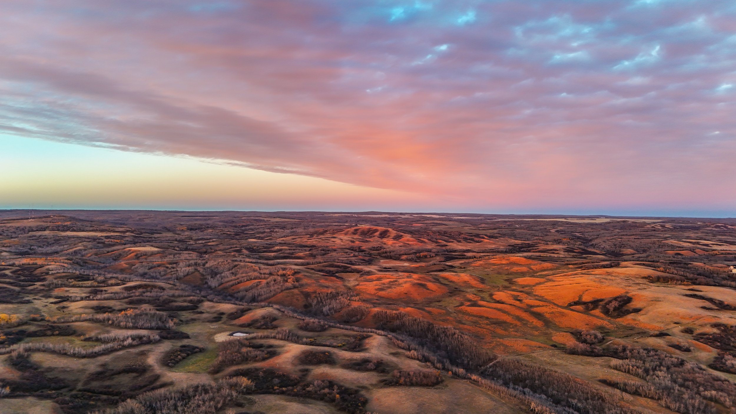 Aerial view of rolling hills and farmland at sunset with colorful sky and clouds
