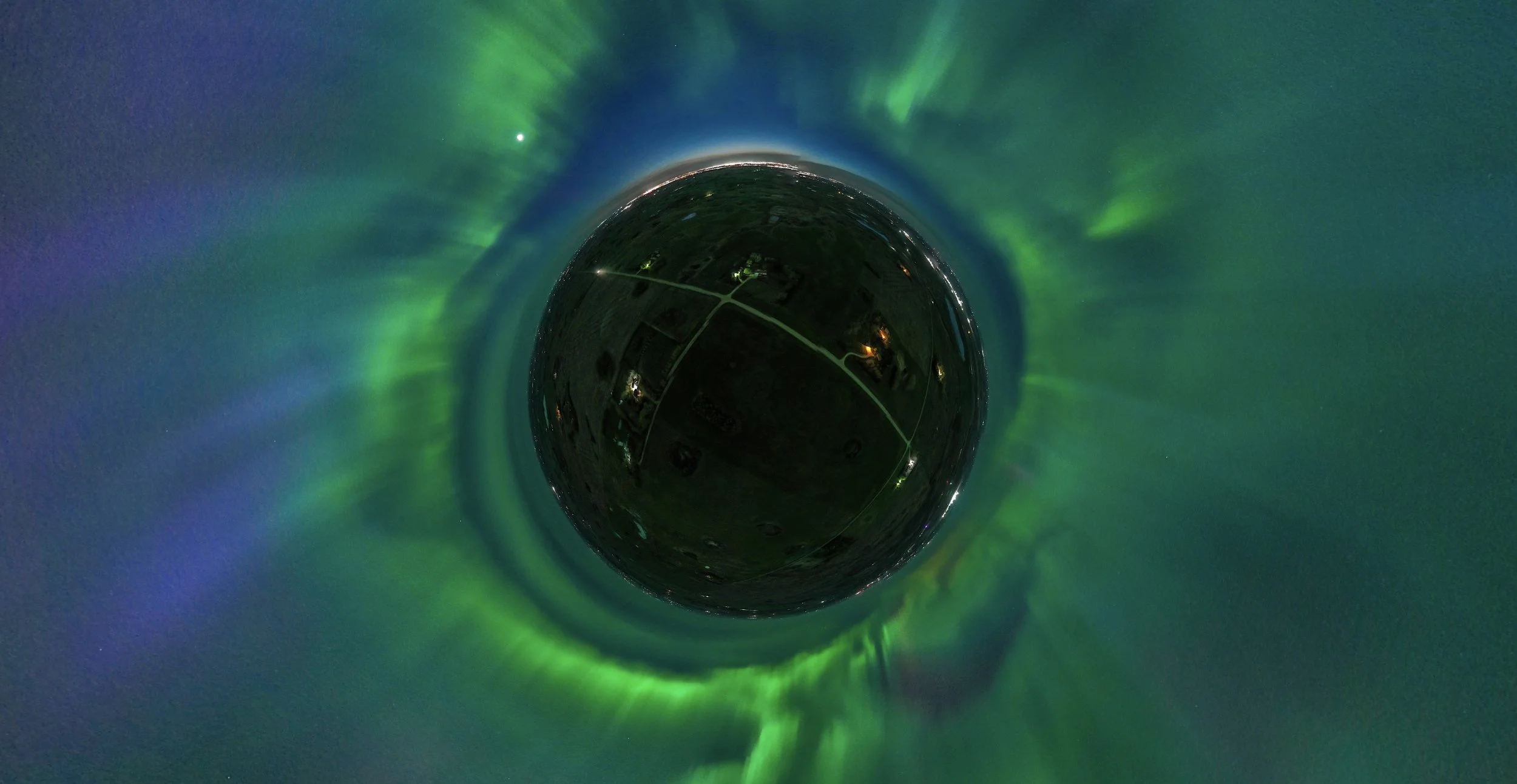 A panoramic, spherical view of the night sky displaying the Northern Lights or Aurora Borealis with green and purple hues, and a bright celestial object, possibly a star or planet, against a dark, starry sky.