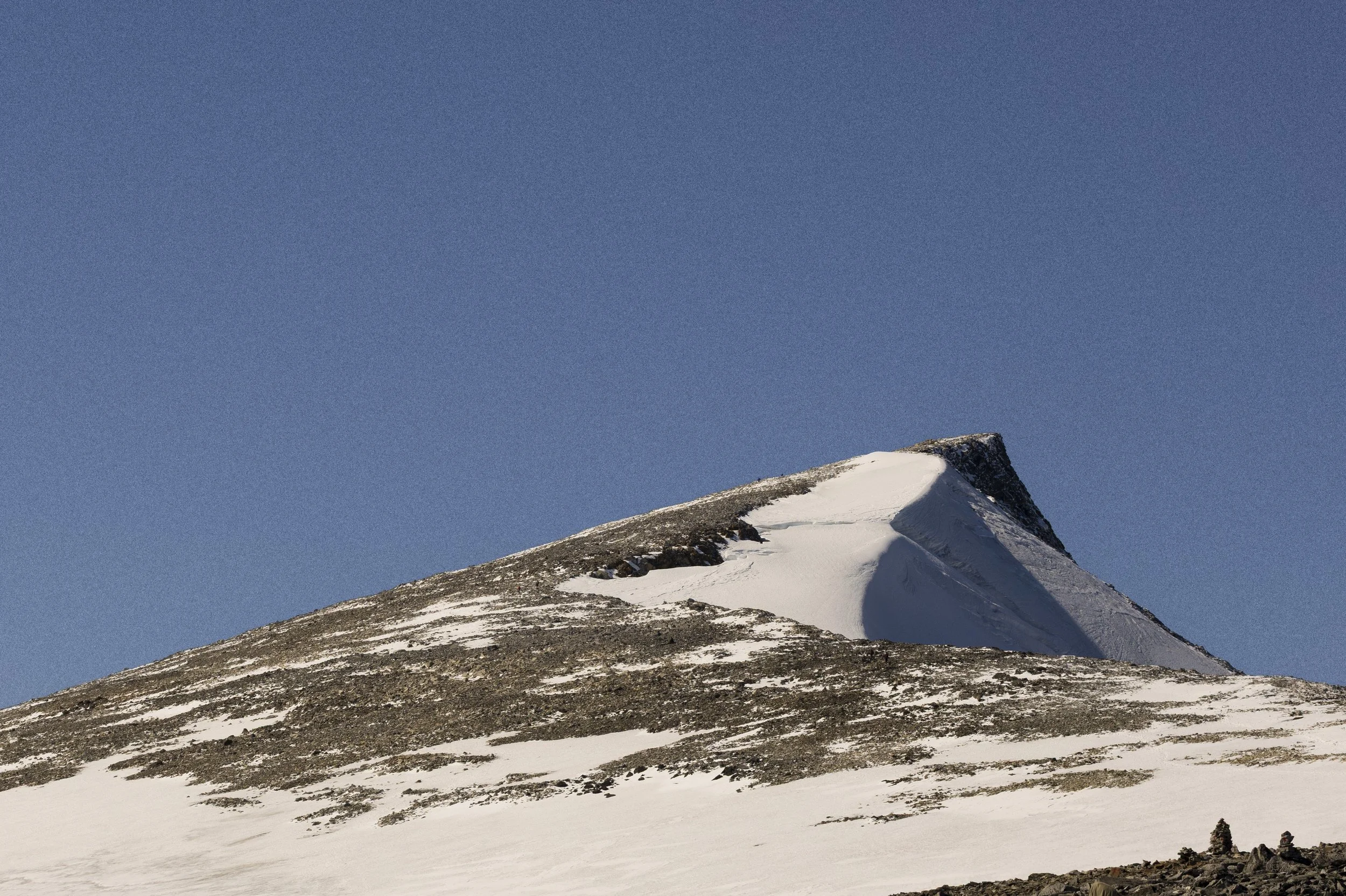 Snow-covered mountain with a sharp peak, under a clear blue sky.