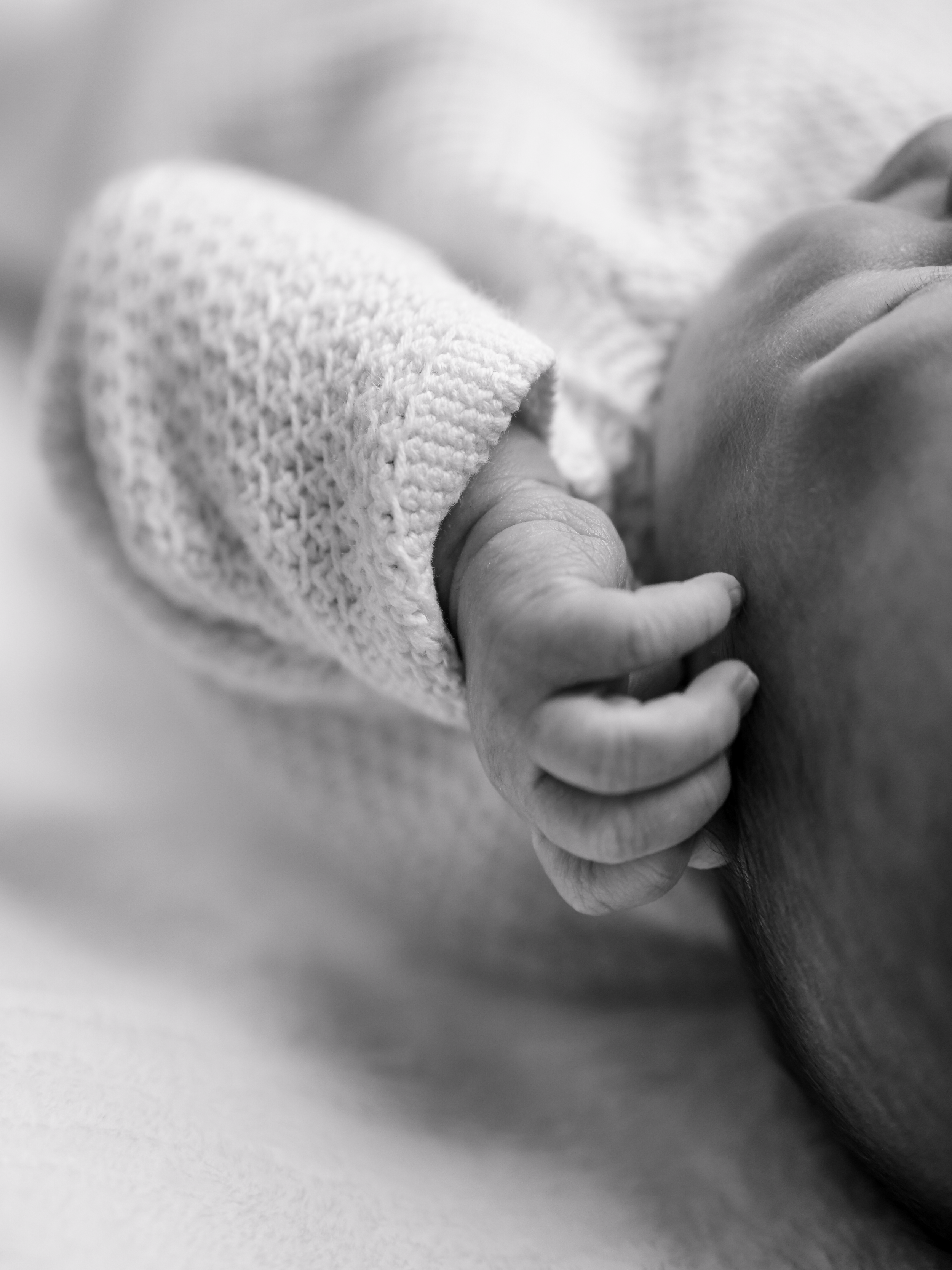 Close-up of a newborn baby's hand gently holding an adult's finger, in black and white.